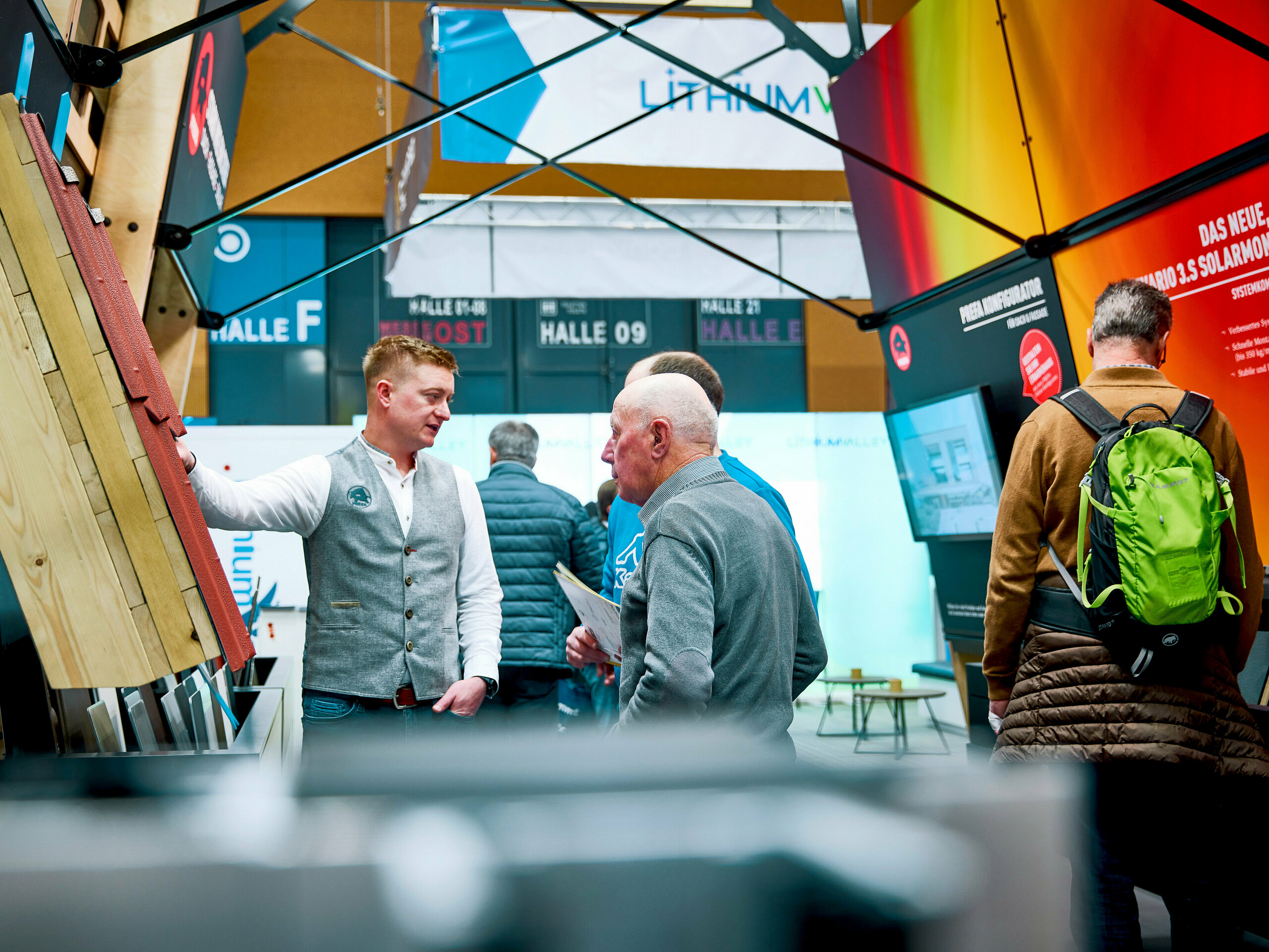 PREFA Messestand 2025 in Wels, Österreich: Felix Gruber, PREFA Gebietsverkaufsleiter, im Gespräch mit interessierten Besuchern, um innovative Lösungen für Dach, Fassade und Solar zu präsentieren. Robuste Aluminiumprodukte überzeugen durch modernes Design und Langlebigkeit. Die persönliche Beratung steht im Zentrum – praxisnah, kompetent und lösungsorientiert. Das attraktive Farbspiel und die hochwertige Materialausstellung ziehen Blicke an. PREFA zeigt sich als starker Partner für Sanierung, Neubau und Energiefragen.