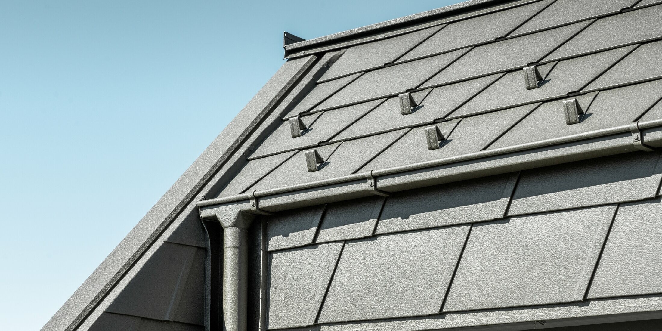 PREFA DS.19 Aluminium-Dachschindeln mit Schneestopper. Die Dachentwässerung erfolgt über das PREFA Quadratrohr und Ablaufrohr in der Farbe P.10 Braun.