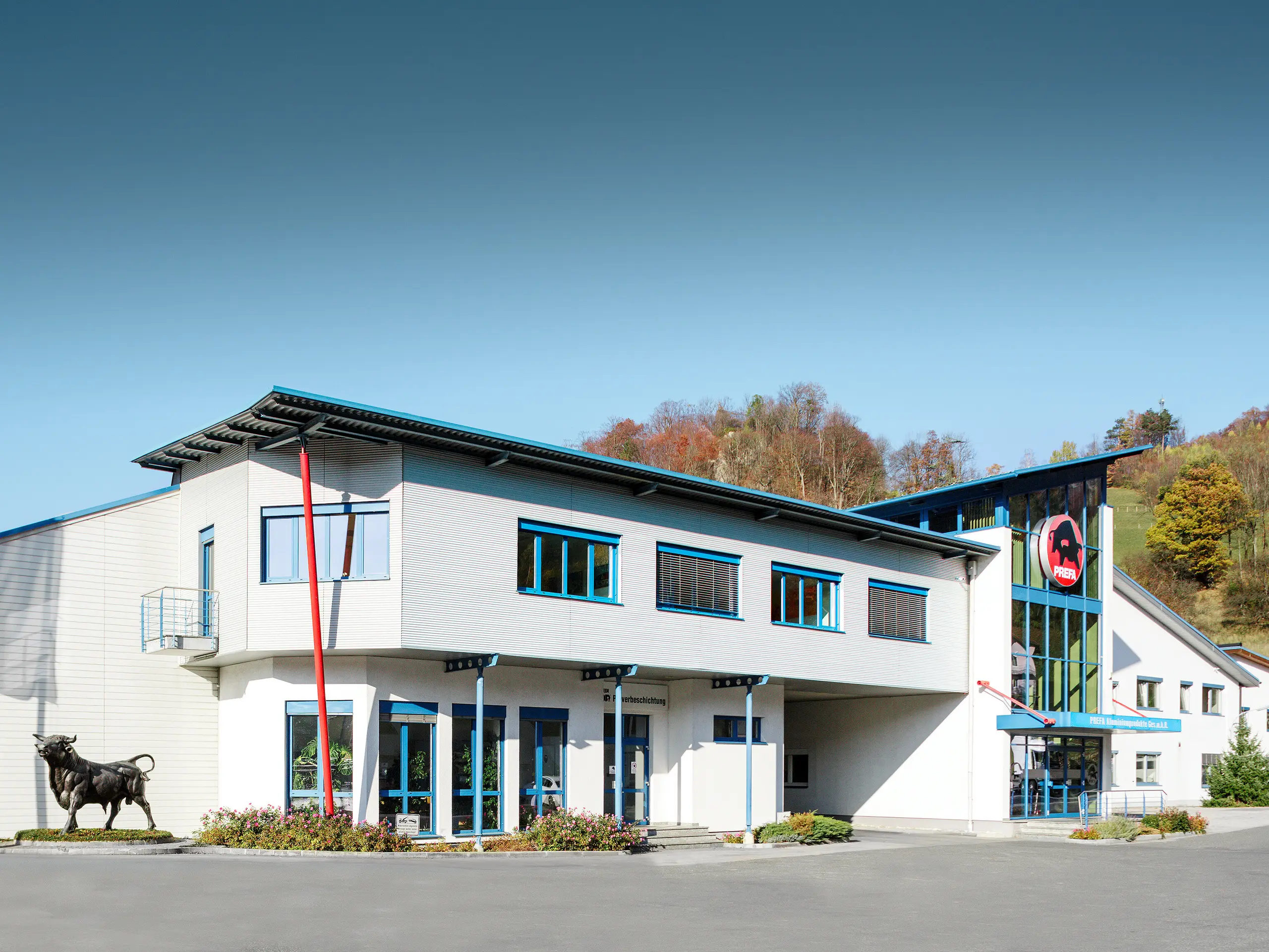 Der PREFA Standort Marktl beeindruckt mit moderner Architektur, markantem PREFA-Stier, großflächiger Glasfassade und einer weithin sichtbaren Fahne mit dem Slogan „Stark wie ein Stier.“