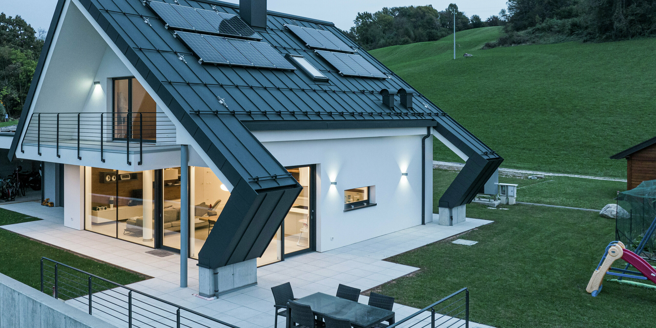 Modernes Einfamilienhaus in Borgo Valbelluna mit PREFALZ Stehfalzdeckung in P.10 Anthrazit. Das markante Aluminiumdach und die darauf montierten Photovoltaikmodule verbinden Ästhetik und Nachhaltigkeit. Die weit auskragenden Dachflächen bieten zusätzlichen Schutz für die Fassade und die großzügige Terrasse. Große Glasflächen sorgen für eine lichtdurchflutete Wohnatmosphäre, der umlaufende Balkon unterstreicht das elegante Design.