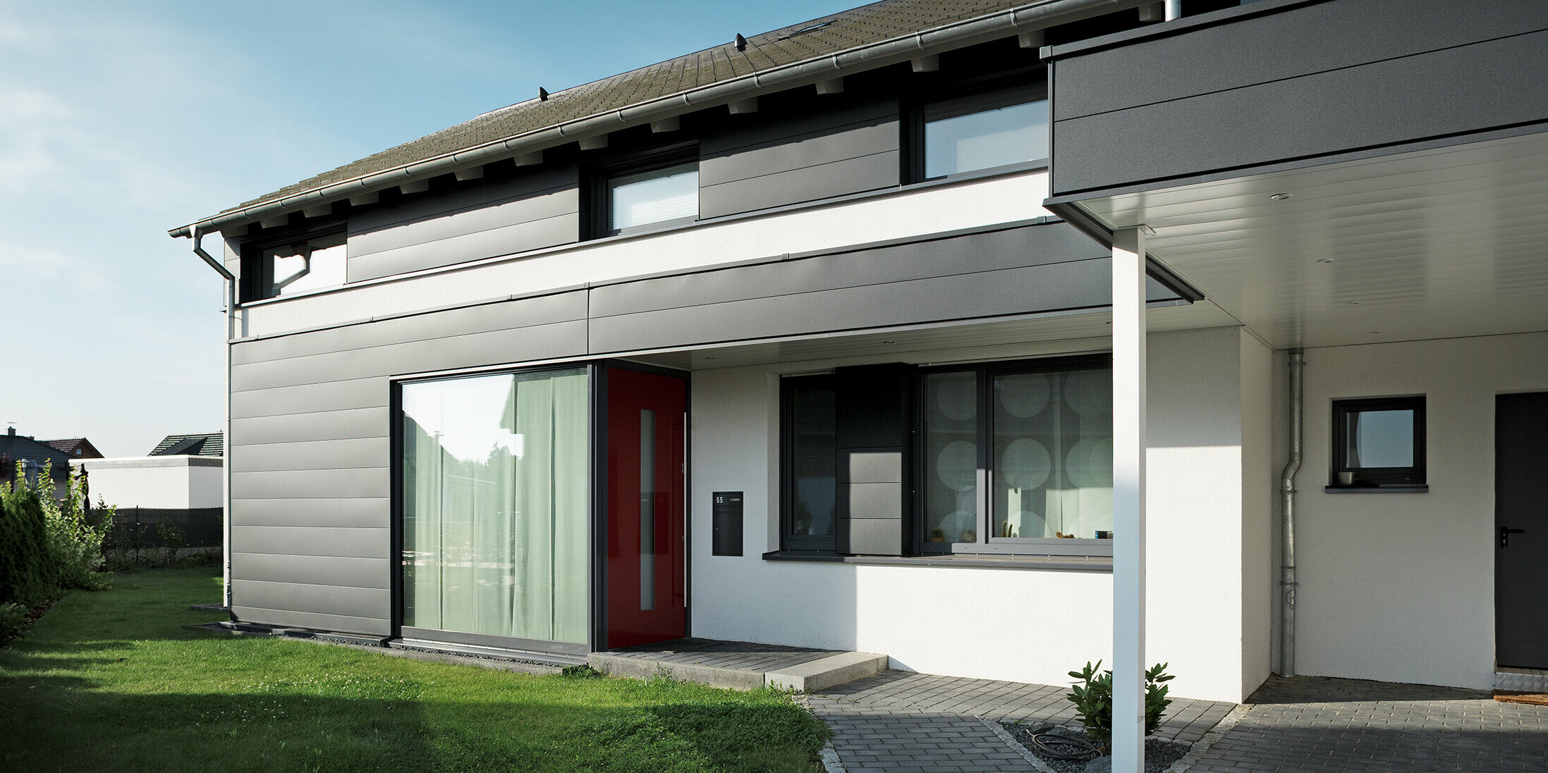 Rückseite eines modernen Einfamilienhauses in Isenbüttel, ausgestattet mit PREFA Aluminium-Sidings in P.10 Anthrazit – ein perfektes Zusammenspiel von Funktionalität und Ästhetik. Die großzügigen Fenster sorgen für ein optisches Highlight und lichtdurchflutete Innenräume.