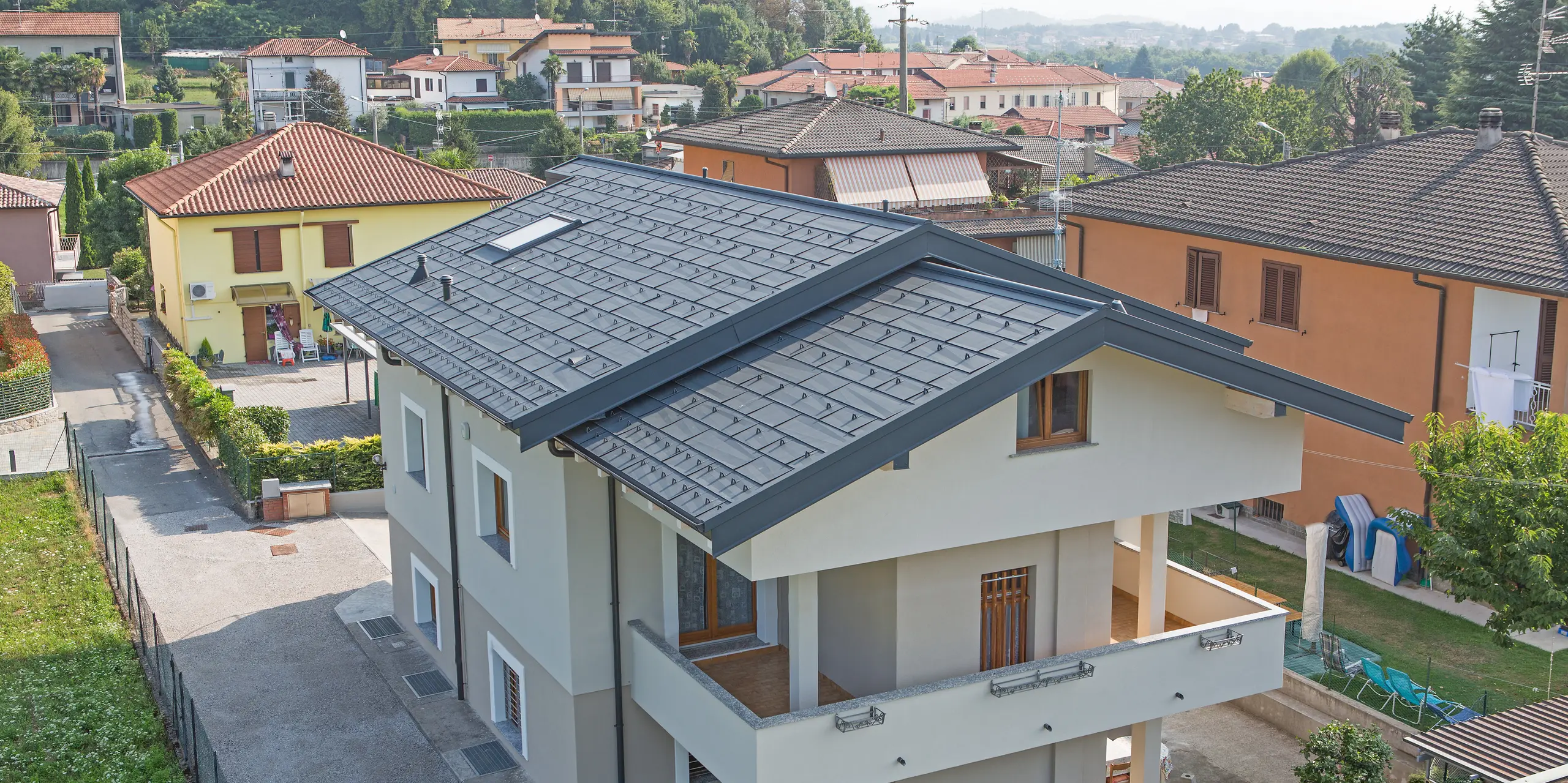 Detailaufnahme des PREFA Dachs FX.12 in P.10 Anthrazit auf einem Einfamilienhaus in Beregazzo, Italien. Die markanten, unregelmäßig gekanteten Aluminium-Dachpaneele erzeugen ein faszinierendes geometrisches Muster und ein dynamisches Lichtspiel. Die elegante Dachfläche vereint moderne Architektur mit den Vorteilen von PREFA Aluminium: langlebig, witterungsbeständig und optisch außergewöhnlich.