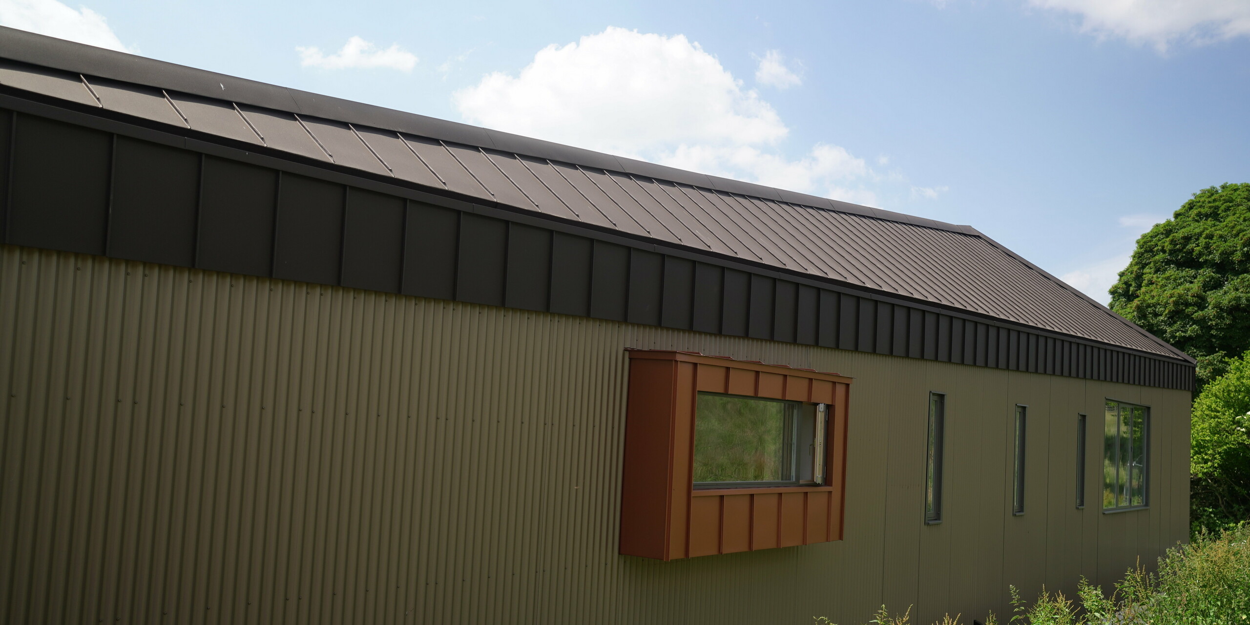 Langhaus mit Aluminium-Dach aus PREFALZ in P.10 Braun und Fensterverkleidung aus Falzonal in der Farbe Neukupfer
