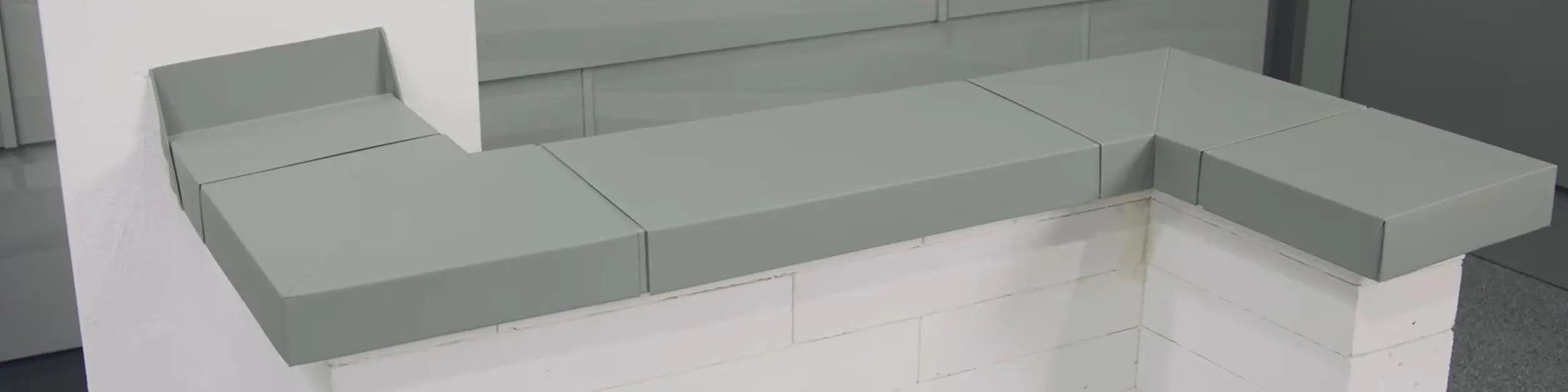 Graue PREFA Mauerabdeckung aus Aluminium auf weißem Mauerwerk mit moderner Fassadenverkleidung im Hintergrund