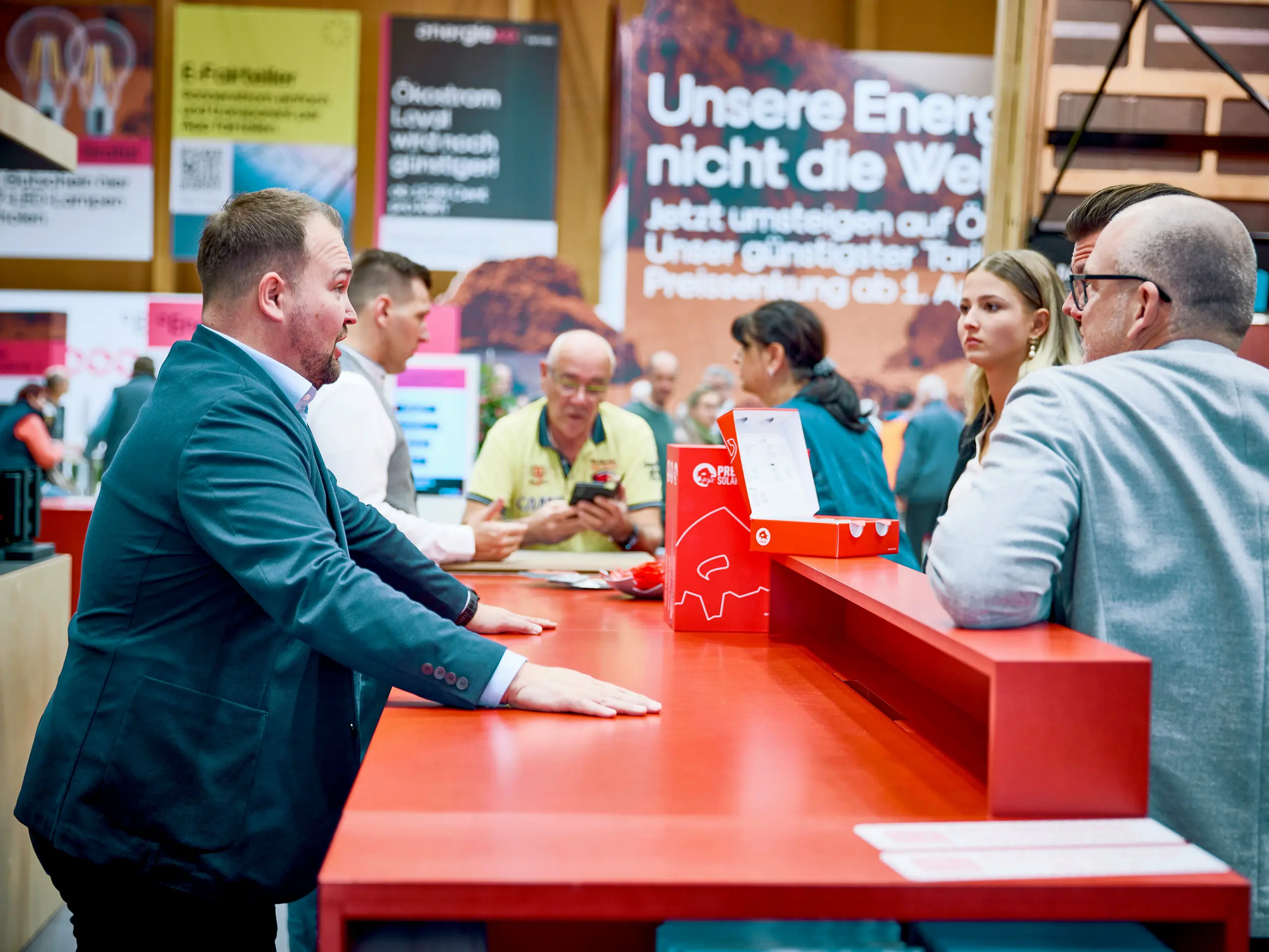 Persönliche Beratung am PREFA Messestand 2026: In intensiven Gesprächen mit Fachbesuchern erläutert Jürgen Bauer, Marketing Koordinator Österreich, individuelle Lösungen für Dach, Fassade und Solar. Die leuchtend rote Beratungstheke mit dem ikonischen Stier-Logo ist zentraler Treffpunkt für Bauherren, Planer und Verarbeiter. Der direkte Austausch schafft Vertrauen, klärt technische Fragen und unterstützt bei der Projektplanung. PREFA setzt auf Dialog statt Informationsflut – mit praxisnahen Antworten, kompetenter Beratung und innovativen Produkten für energieeffizientes und langlebiges Bauen.