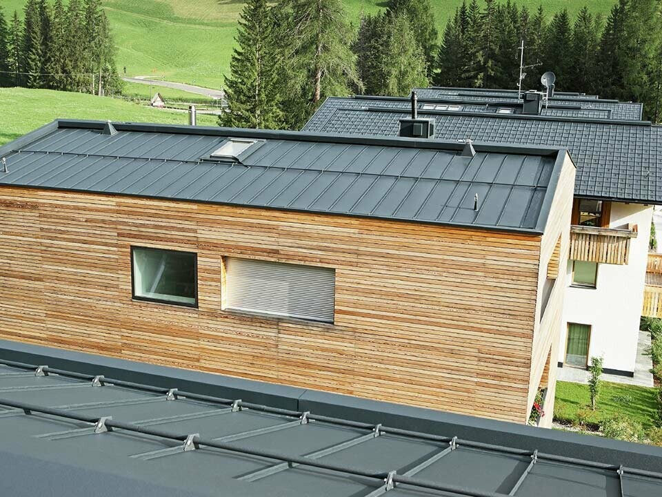 Wohnbauten in Corvara, eingedeckt mit Doppelstehfalzdächer in Anthrazit von PREFA und einer Holzfassade liegend verlegt.