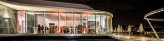 Nachtaufnahme der Libelle MQ auf dem Dach des Leopold Museums mit einer spiegelnden Fläche, die Gäste befinden sich im erleuchteten Veranstaltungsraum.