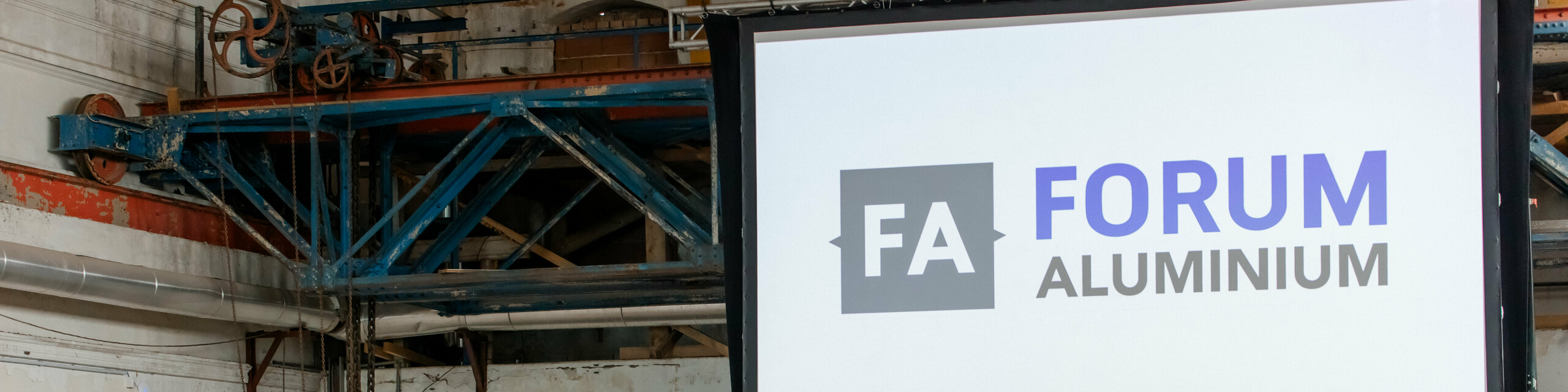Große Bühne beim Forum Aluminium mit beeindruckender Leinwand und „FA Forum Aluminium“-Logo als zentralem Eyecatcher. Vor industrieller Kulisse des Glanzstoff-Geländes in St. Pölten spricht Dr. Cornelius Alexander Grupp am Rednerpult zu einem dicht besetzten Publikum aus Branchenexperten und Entscheidern. Banner zu Aluminiumlösungen und innovative Anwendungen unterstreichen die thematische Tiefe. Die Szene zeigt den intensiven Austausch zu Zukunftstechnologien, Recycling und Marktentwicklungen und vermittelt die dynamische Atmosphäre einer hochkarätigen Fachkonferenz.