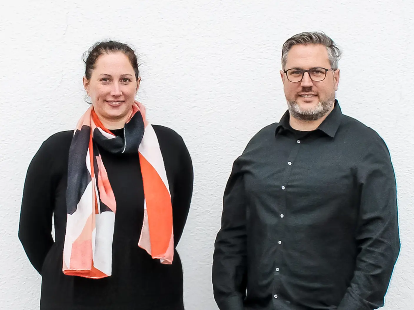 Portrait von den Geschwistern Nathalie und Marc Bodarwé von BODARWE Architektur vor einer weiß verputzten Wand.