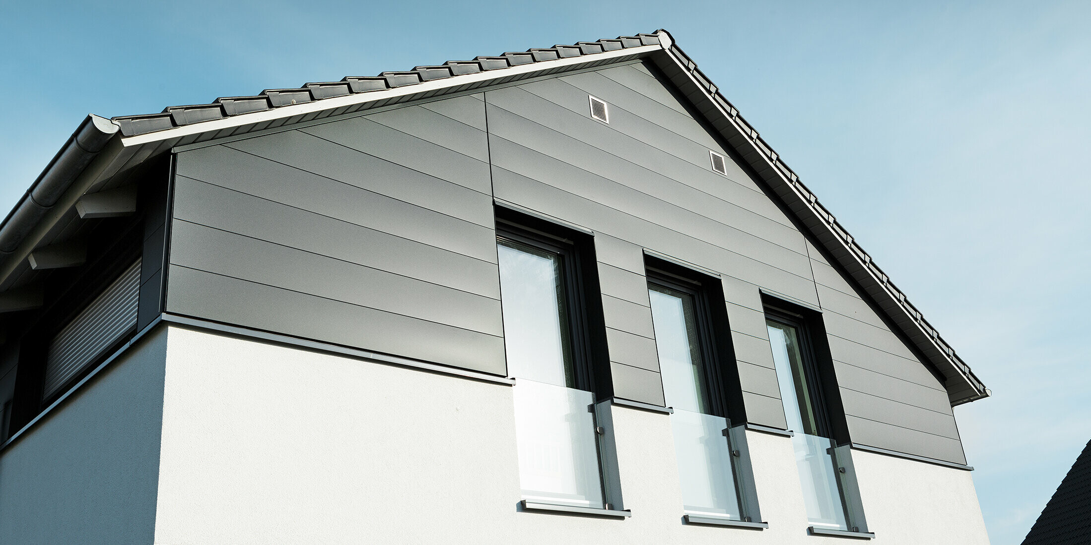 Moderne Hausfassade in Isenbüttel mit PREFA Sidings in P.10 Anthrazit – die Aluminiumverkleidung verleiht dem Einfamilienhaus einen eleganten und wetterfesten Look. Die vertikalen Fenster betonen die moderne Architektur zusätzlich.