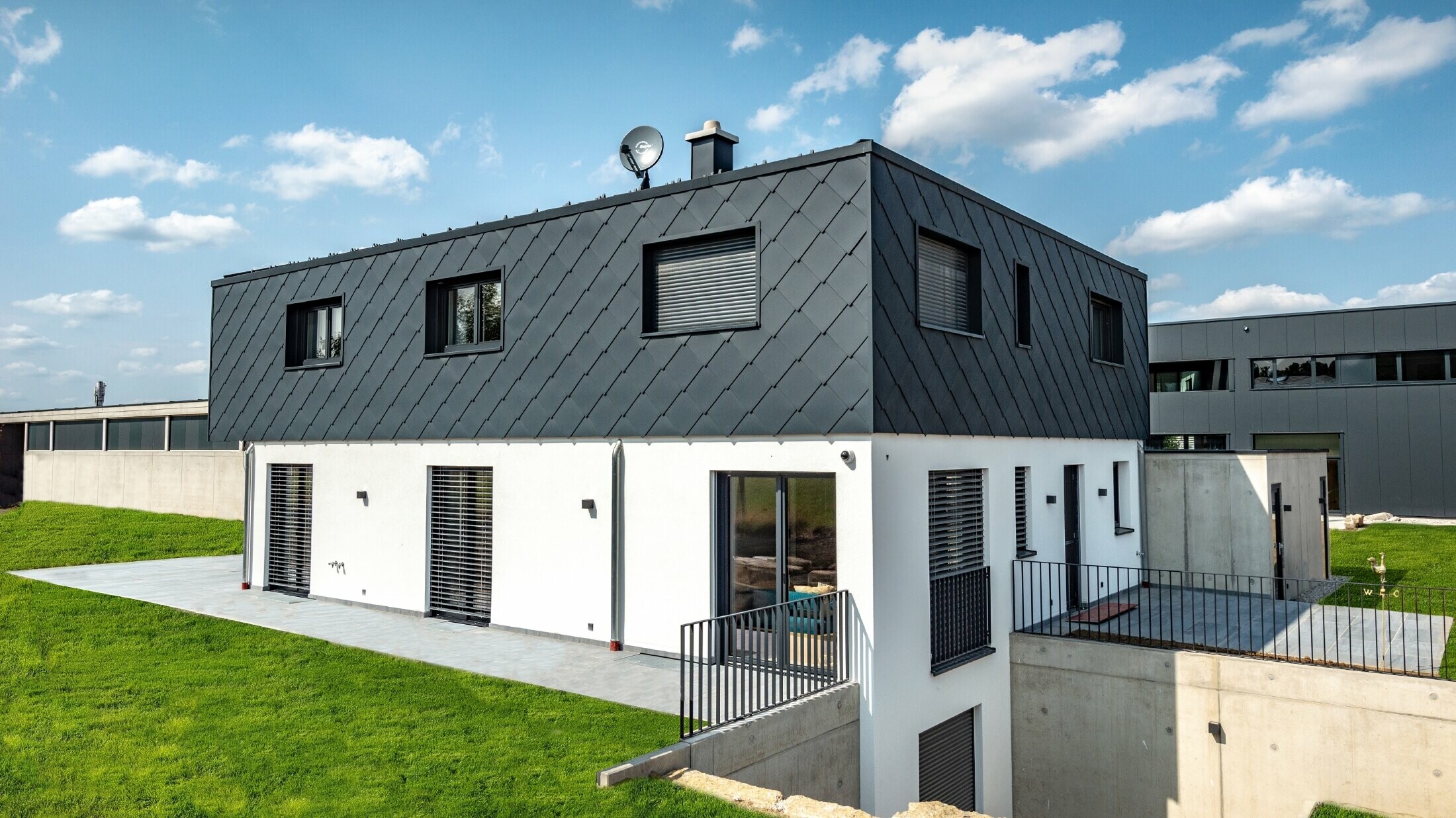 Schlichter Neubau mit Flachdach, das Erdgeschoß ist weiß verputzt, das Obergeschoß ist mit der großen PREFA Wandraute in Anthrazit verkleidet.