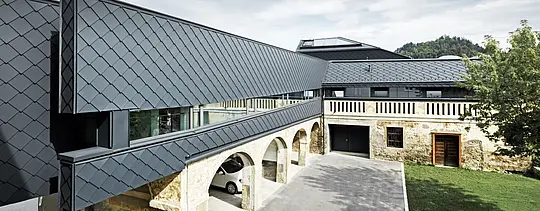 Ein altes Steingemäuer kombiniert mit modernen Fassadenelementen aus PREFA Wandrauten in P.10 Anthrazit