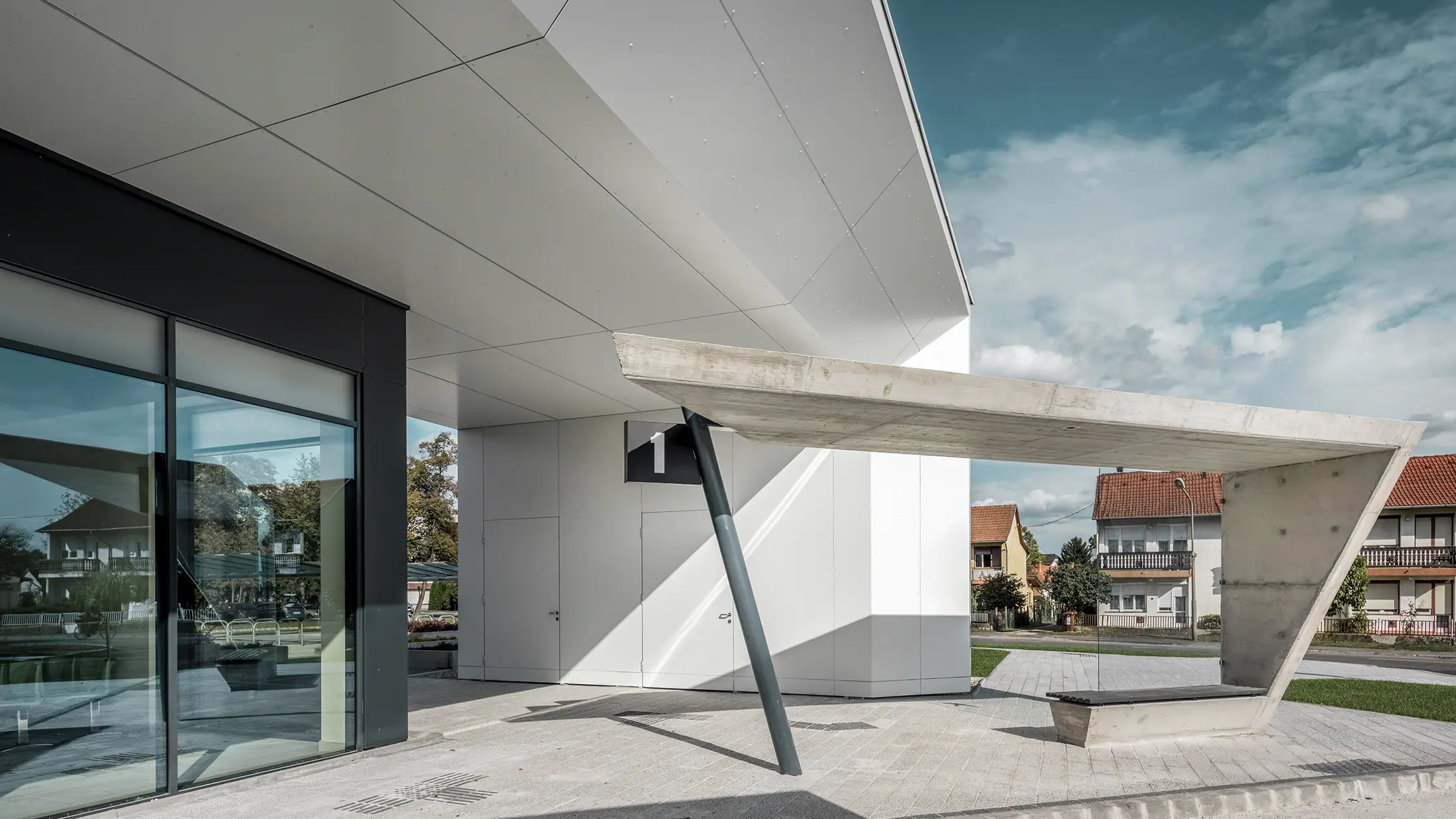 Eingangsbereich des Busbahnhofs Lenti; die Untersicht der Überdachung ist mit der PREFABOND Aluminium Verbundplatte von PREFA in Reinweiß verkleidet, die Fassadenelemente bei den Eingangstüren und Schaufenstern ist in P.10 anthrazit verkleidet.