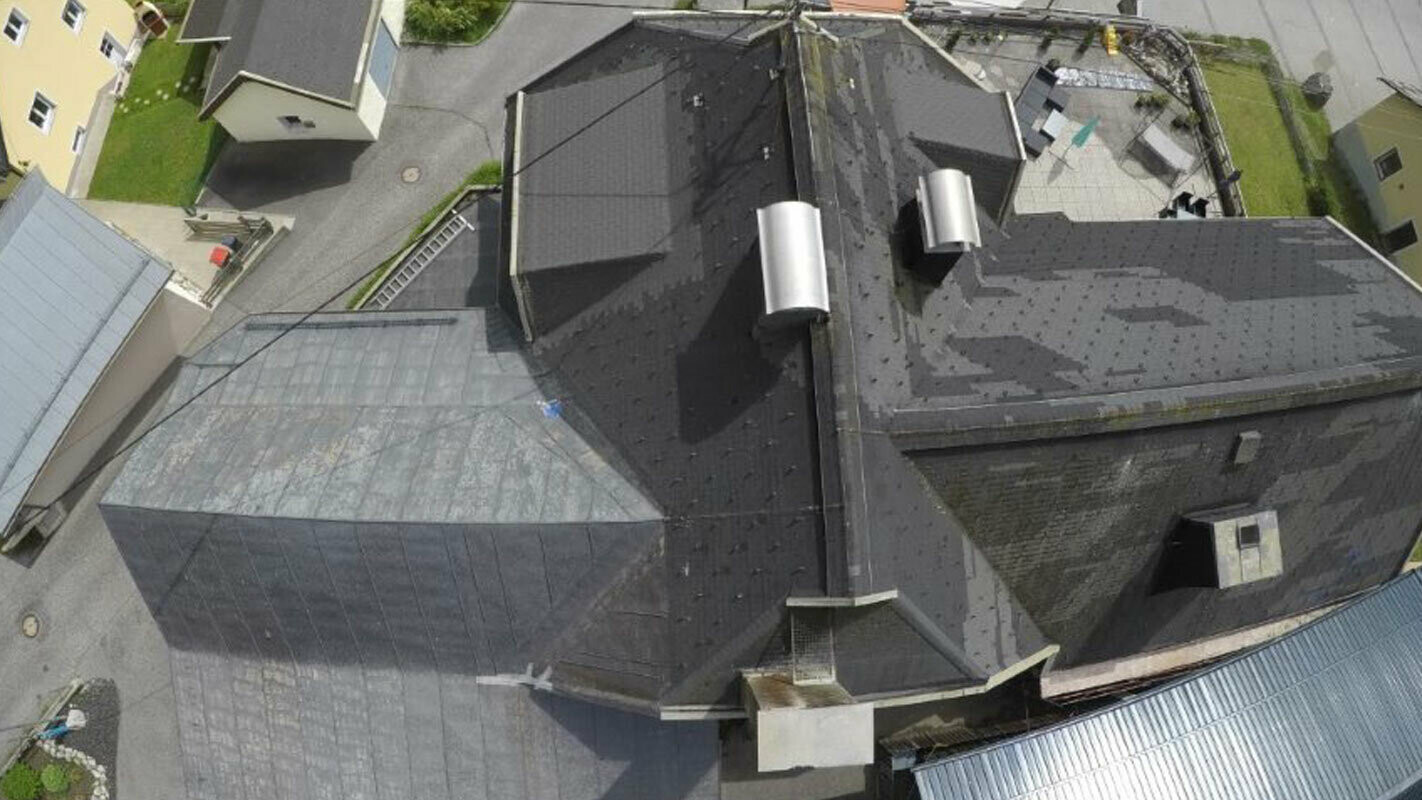 Vogelperspektive eines alten Daches mit vielen Datails - Kehlen, Gauben und Kamine. Die alte Dacheindeckung wurde mehrfach ausgebessert und ist fleckig.