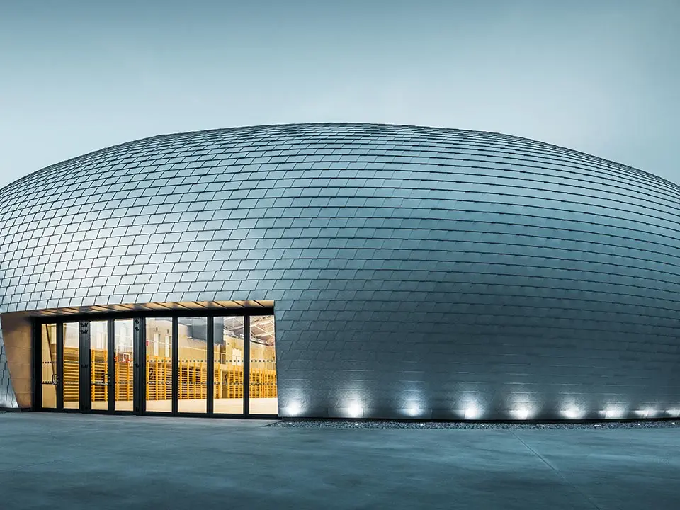 Die Sporthalle in Tschechien erinnert in ihrer Form an ein UFO - dazu wurden 20.000 PREFA Wandschindeln in Naturblank verlegt