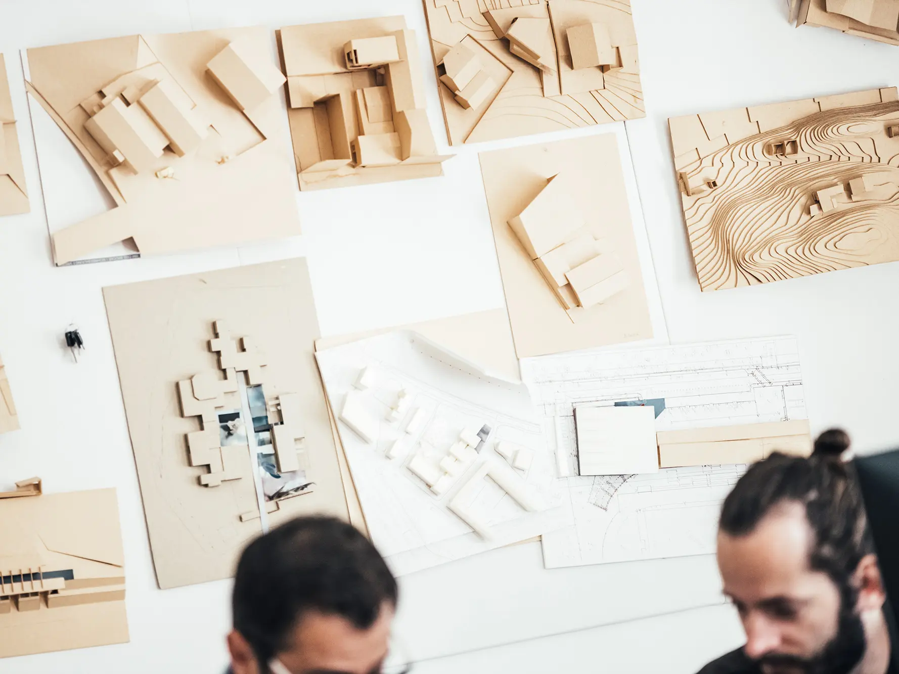 Aufnahme von Architekturmodellen an der Wand. Unscharf im Vordergrund: zwei Mitarbeiter des Büros.
