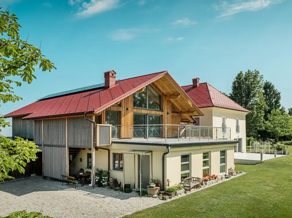 Die beiden sanierten Einfamilienhäuser in Aschach an der Steyr beeindrucken durch ihre harmonische Dachgestaltung. Die PREFA Dachraute 44 x 44 in der Farbe P.10 Oxydrot verleiht ihnen ein markantes, zeitloses Aussehen und bildet einen starken Kontrast zur modernen Holzverkleidung bzw. der gelblichen Putzfassade. Hervorzuheben sind zudem die großflächigen Fenster, welche die Offenheit des Obergeschosses noch verstärken. Das großzügige Grundstück und die gepflegte Gartenlandschaft betonen die gelungene Verbindung von Natur, Tradition und Moderne. Die PREFA Dachrauten sind nicht nur ästhetisch ansprechend, sondern auch äußerst beständig und langlebig – ideal für jedes Wetter.
