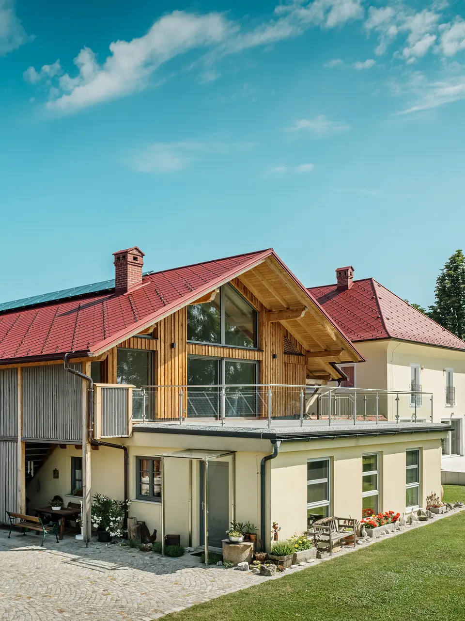 Die beiden sanierten Einfamilienhäuser in Aschach an der Steyr beeindrucken durch ihre harmonische Dachgestaltung. Die PREFA Dachraute 44 x 44 in der Farbe P.10 Oxydrot verleiht ihnen ein markantes, zeitloses Aussehen und bildet einen starken Kontrast zur modernen Holzverkleidung bzw. der gelblichen Putzfassade. Hervorzuheben sind zudem die großflächigen Fenster, welche die Offenheit des Obergeschosses noch verstärken. Das großzügige Grundstück und die gepflegte Gartenlandschaft betonen die gelungene Verbindung von Natur, Tradition und Moderne. Die PREFA Dachrauten sind nicht nur ästhetisch ansprechend, sondern auch äußerst beständig und langlebig – ideal für jedes Wetter.