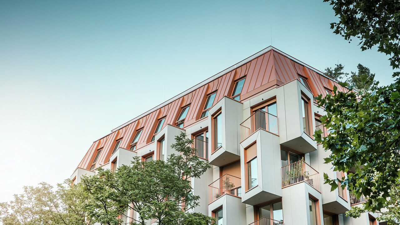 Moderne Wohnarchitektur im Projekt Van B in München mit einem innovativen Erker und einem markanten PREFALZ-Aluminiumdach in der Sonderfarbe IGP Orange HDP von PREFA. Das hochwertige Dachmaterial überzeugt durch seine außergewöhnliche Langlebigkeit, hohe Widerstandsfähigkeit und Farbstabilität. In Kombination mit der kubischen Fassadenform und den großflächigen Glasfronten entsteht ein harmonisches Gesamtbild, das Funktionalität, Design und Nachhaltigkeit auf höchstem Niveau vereint – ideal für urbanes Wohnen.
