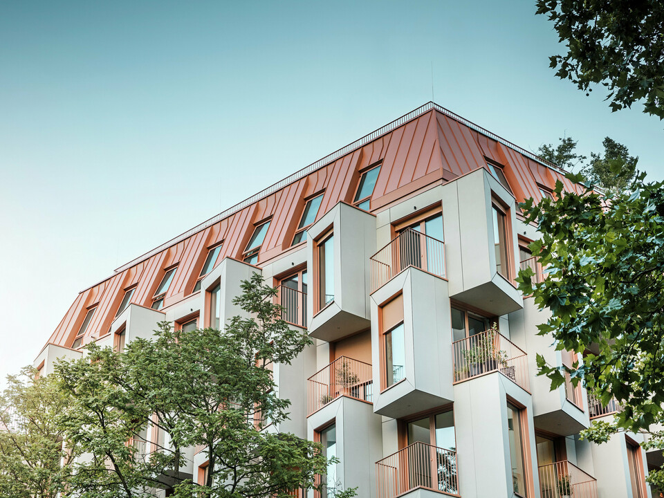 Moderne Wohnarchitektur beim Projekt Van B in München mit innovativer Erkerfassade und markantem PREFALZ Aluminiumdach in der Sonderfarbe IGP Orange HDP von PREFA. Das hochwertige Dachmaterial überzeugt durch extreme Langlebigkeit, hohe Widerstandsfähigkeit und Farbbeständigkeit. In Kombination mit der kubischen Fassadengestaltung und den großen Fensterflächen entsteht ein harmonisches Gesamtbild, das Funktionalität, Design und Nachhaltigkeit auf höchstem Niveau vereint - ideal für urbanes Wohnen.
