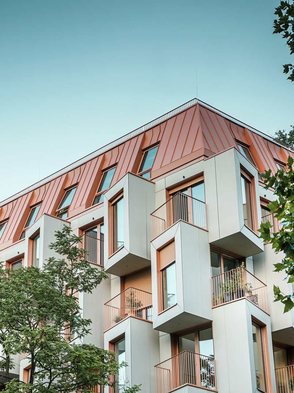 Moderne Wohnarchitektur beim Projekt Van B in München mit innovativer Erkerfassade und markantem PREFALZ Aluminiumdach in der Sonderfarbe IGP Orange HDP von PREFA. Das hochwertige Dachmaterial überzeugt durch extreme Langlebigkeit, hohe Widerstandsfähigkeit und Farbbeständigkeit. In Kombination mit der kubischen Fassadengestaltung und den großen Fensterflächen entsteht ein harmonisches Gesamtbild, das Funktionalität, Design und Nachhaltigkeit auf höchstem Niveau vereint - ideal für urbanes Wohnen.