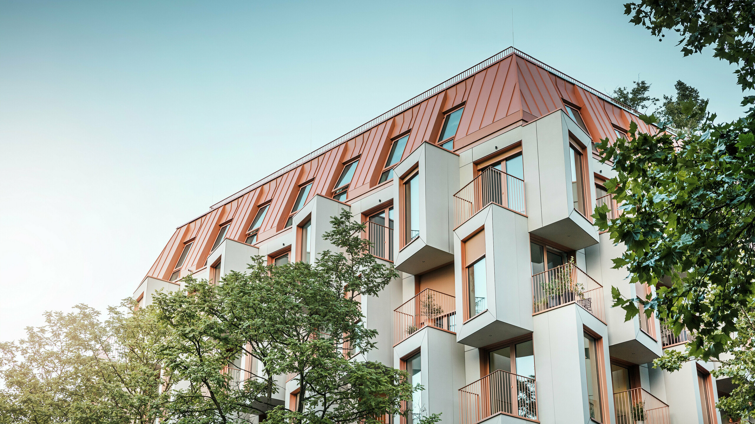 Moderne Wohnarchitektur beim Projekt Van B in München mit innovativer Erkerfassade und markantem PREFALZ Aluminiumdach in der Sonderfarbe IGP Orange HDP von PREFA. Das hochwertige Dachmaterial überzeugt durch extreme Langlebigkeit, hohe Widerstandsfähigkeit und Farbbeständigkeit. In Kombination mit der kubischen Fassadengestaltung und den großen Fensterflächen entsteht ein harmonisches Gesamtbild, das Funktionalität, Design und Nachhaltigkeit auf höchstem Niveau vereint - ideal für urbanes Wohnen.