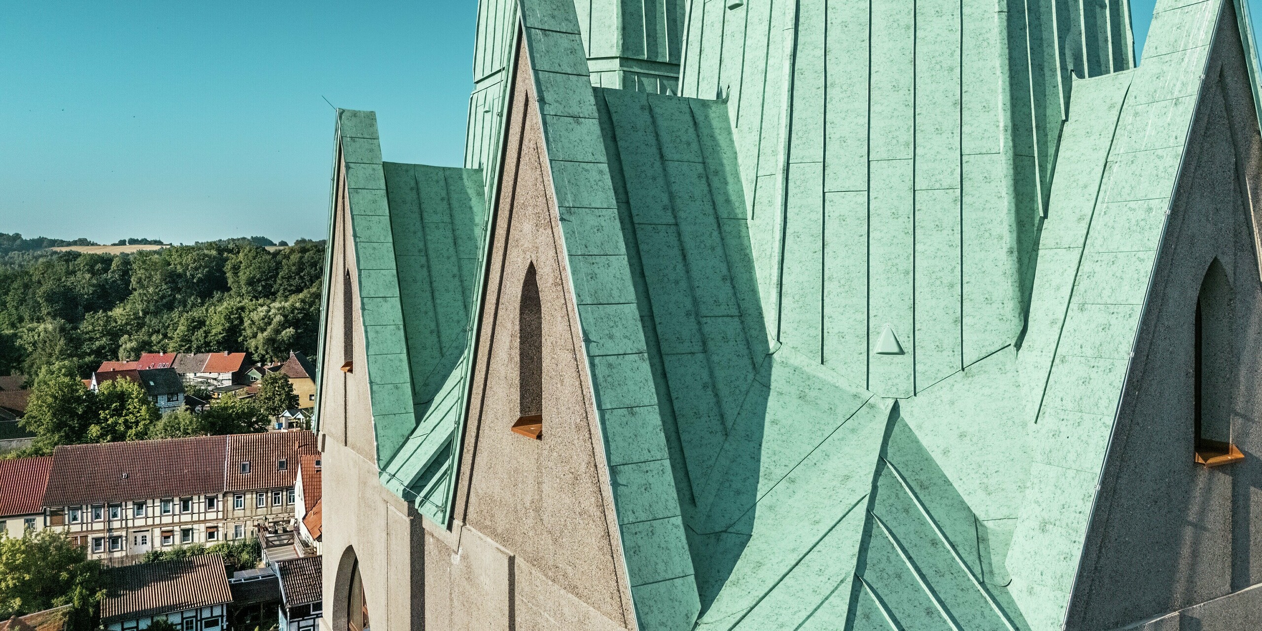etailaufnahme des neu errichteten Kirchturms des Tourismuszentrums Ellrich: Die präzise ausgeführten Falzlinien aus PREFALZ Aluminium in der Farbe P.10 Patinagrün ziehen alle Blicke auf sich. Die Oberfläche schimmert im Sonnenlicht und unterstreicht die moderne Interpretation historischer Architektur. PREFALZ ist robust, langlebig, wartungsarm und aufgrund seiner flexiblen Verarbeitungsmöglichkeiten perfekt für anspruchsvolle Dachgeometrien geeignet.