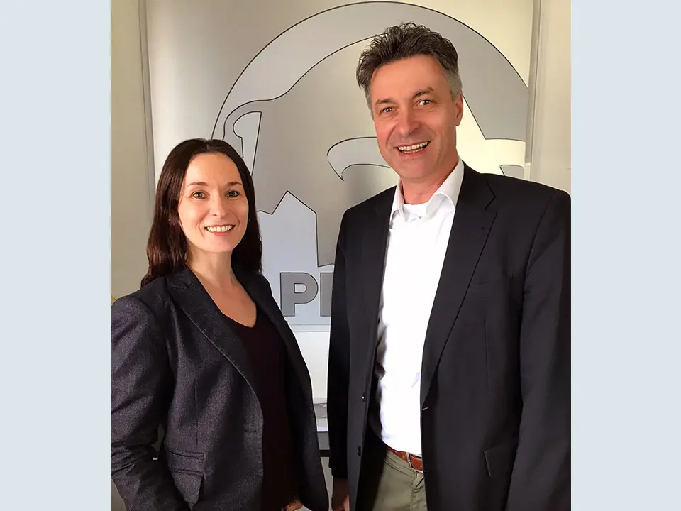die beiden neuen Vertriebsleier, Ursula Obernosterer und Bernhard Dorn, vor dem PREFA Stier Logo mit dunklem Sakko fotografiert