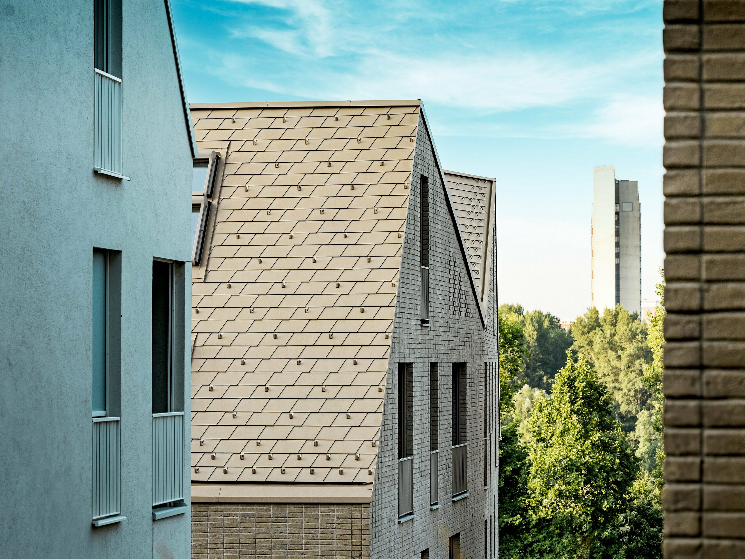 Detailaufnahme der markanten Dachlandschaft im Quartier Vydrica in Bratislava: Steil geneigte Dächer mit präzise verlegten PREFA Aluminium Dachschindeln in P.10 Sandbraun ziehen als rhythmisches Muster alle Blicke auf sich. Die feinen Linien, klaren Kanten und perfekt ausgeführten Anschlüsse zwischen Dach und Fassade unterstreichen die architektonische Qualität. PREFA Aluminium überzeugt durch hohe Formbarkeit für komplexe Geometrien, extreme Witterungsbeständigkeit sowie langlebige, wartungsarme Eigenschaften – ideal für anspruchsvolle urbane Bauprojekte mit starkem Designanspruch.