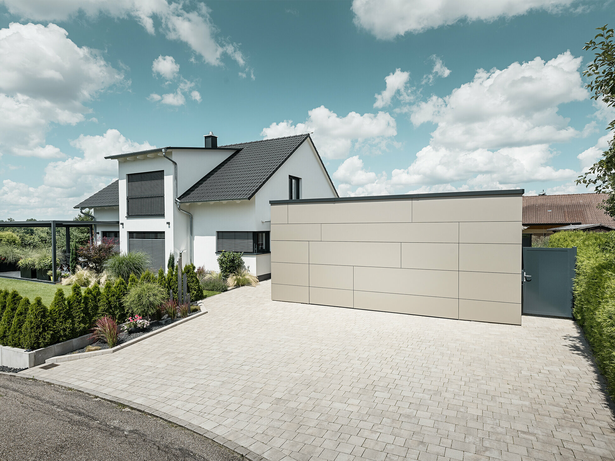 Die Garage des Einfamilienhauses ist an der Fassade komplett mit der Aluminium Verbundplatte in Bronze verkleidet. Auch das Garagentor ist mit den Fugen nicht erkennbar. Davor ist eine großzügige Einfahrt.