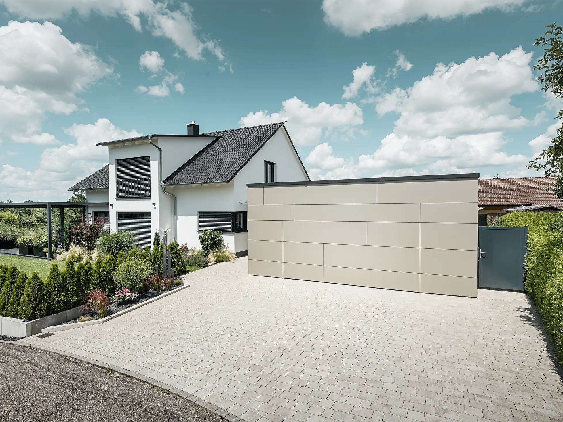 Die Garage des Einfamilienhauses ist an der Fassade komplett mit der Aluminium Verbundplatte in Bronze verkleidet. Auch das Garagentor ist mit den Fugen nicht erkennbar. Davor ist eine großzügige Einfahrt. 