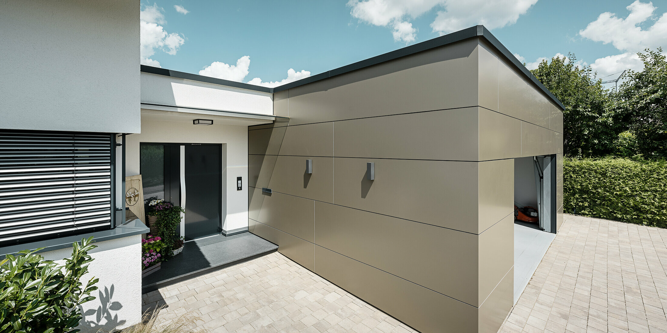 Seitliche Ansicht einer Garage mit PREFABOND Aluminium Verbundplatten in Bronze an der Fassade. Man sieht auch den Eingangsbereich des Hauses.