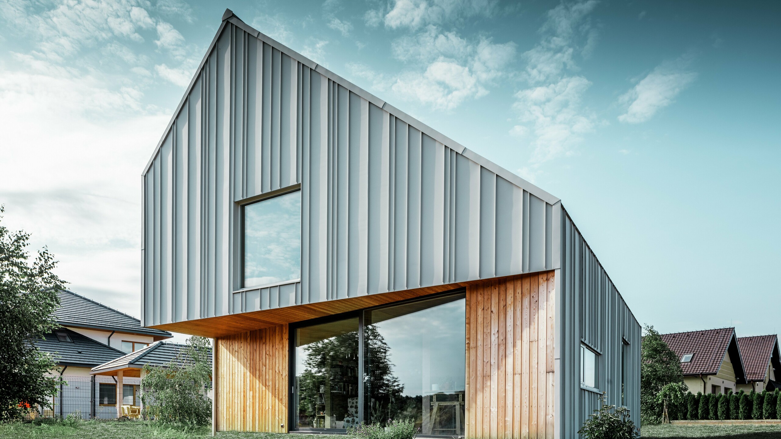 Modernes Einfamilienhaus mit Satteldach ohne Dachvorsprung und Aluminium-Fassade von PREFA in weiss. Dazu wird im Erdgeschoss eine Holzfassade mit vertikalen Holzpaneelen kombiniert. 