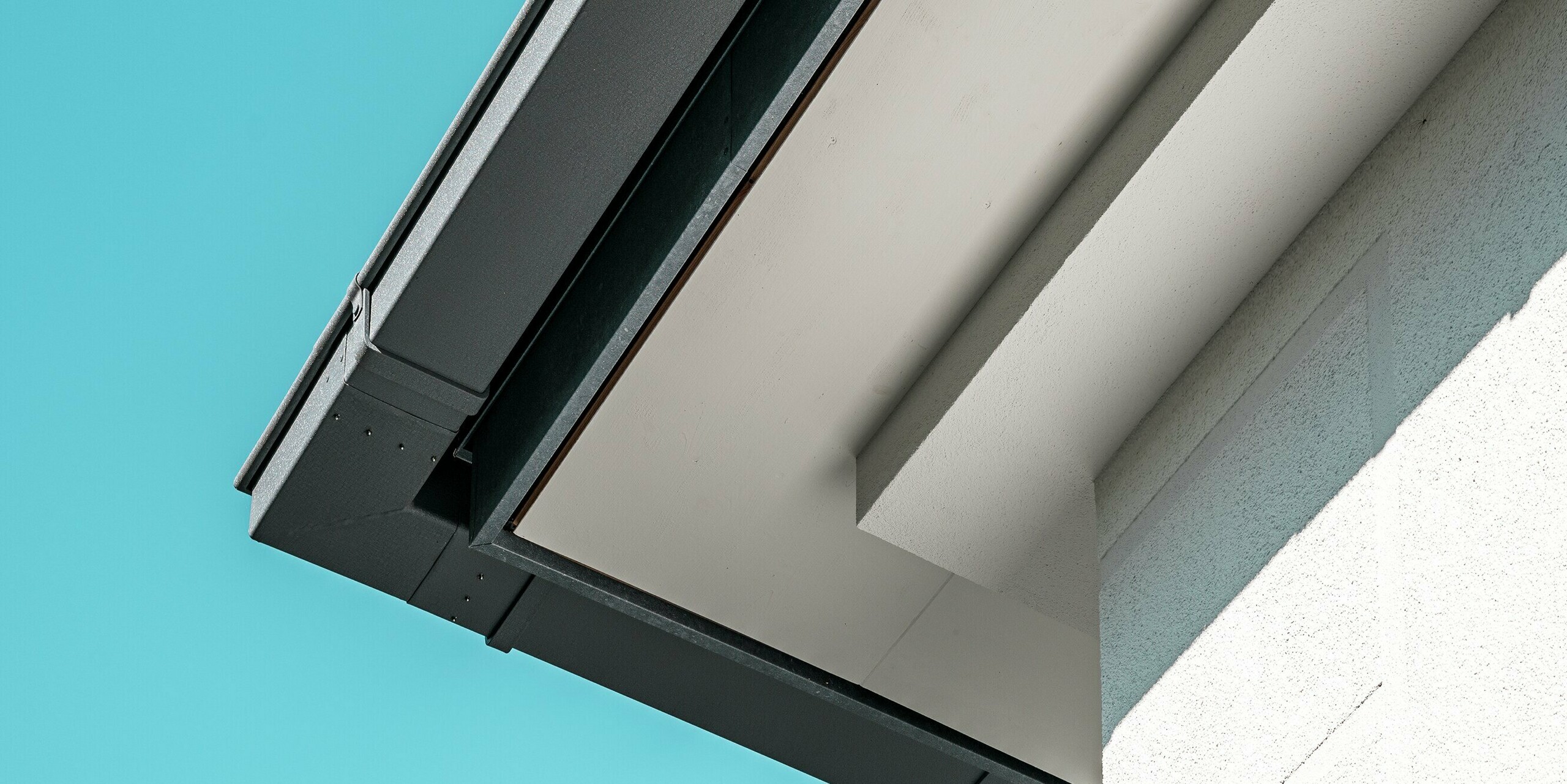 Detailaufnahme der hochwertigen PREFA Kastenrinne in P.10 Steingrau, die für eine effiziente Dachentwässerung sorgt. Das Aluminium-System bietet sowohl ästhetische als auch funktionale Vorteile. Die klare, präzise Linienführung der Rinne und das minimalistische Design ergänzen das elegante Erscheinungsbild des Wohnhauses.