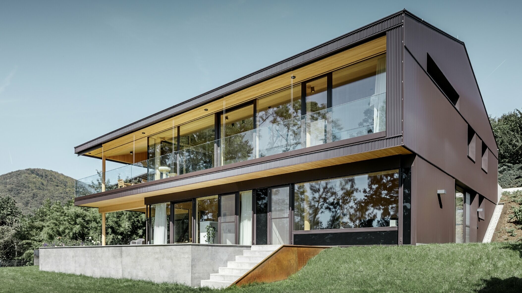 Modernes Einfamilienhaus mit großen Fenstern auf der Gartenseite, die Fassade wurde mit dem PREFA Zackenprofil in dunklem Braun bekleidet.