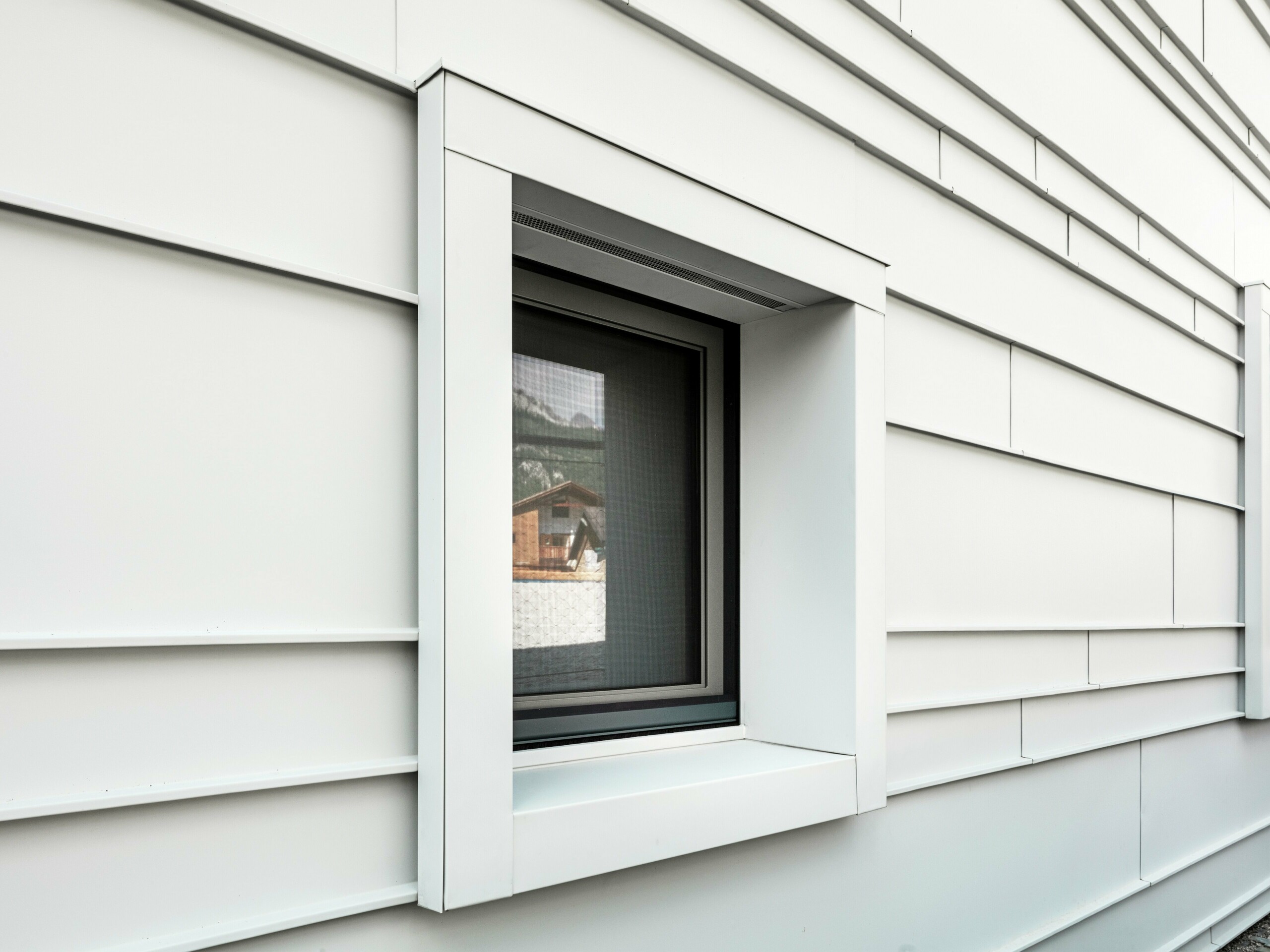 Detailaufnahme eines markanten Fensterausschnitts in einer hinterlüfteten Fassade aus PREFALZ P.10 in der Farbe Prefaweiß. Die horizontal verlegten Aluminiumscharen sorgen für Struktur, Klarheit und eine moderne Ästhetik. Die markant hervortretenden Fensterrahmen der Kaserne „Tempesti” beginnen und enden immer genau an einer Falzlinie. Dadurch wird die Struktur des Aluminiums bewusst hervorgehoben.