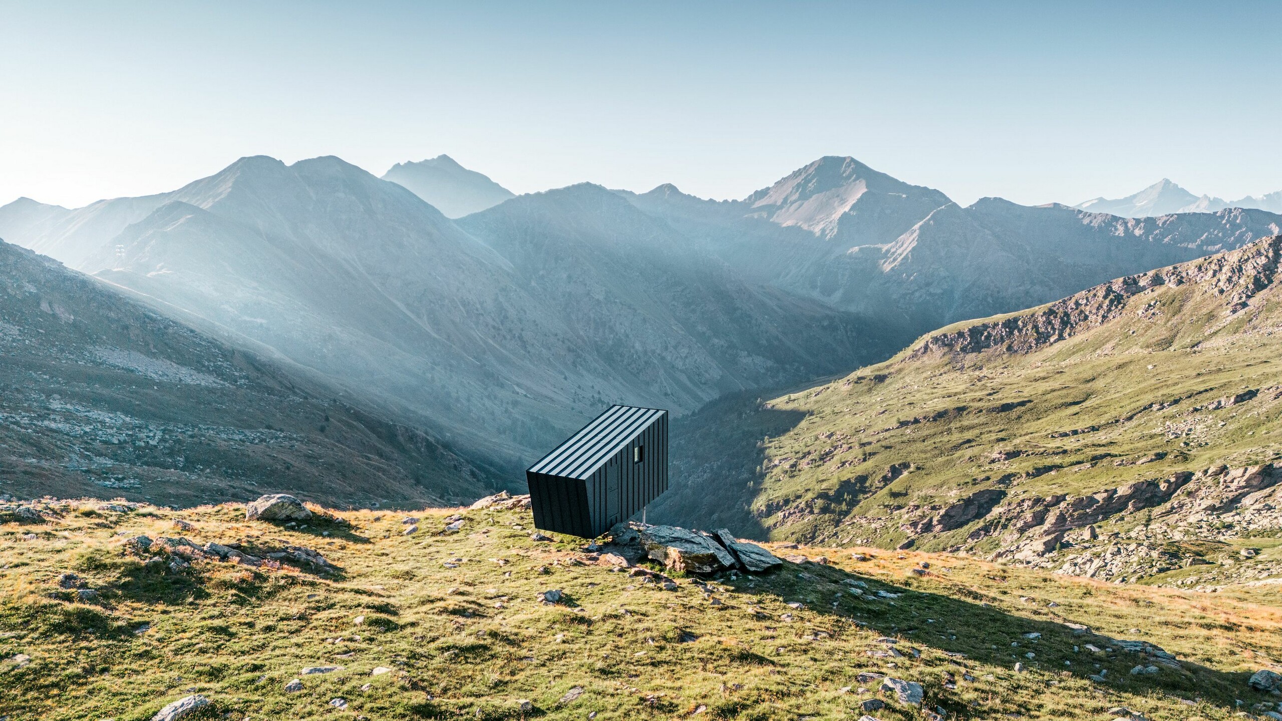 Das Gebäude, ausgerichtet auf die verschneiten Bergspitzen, von der seitlichen Rückseite aus der Distanz.