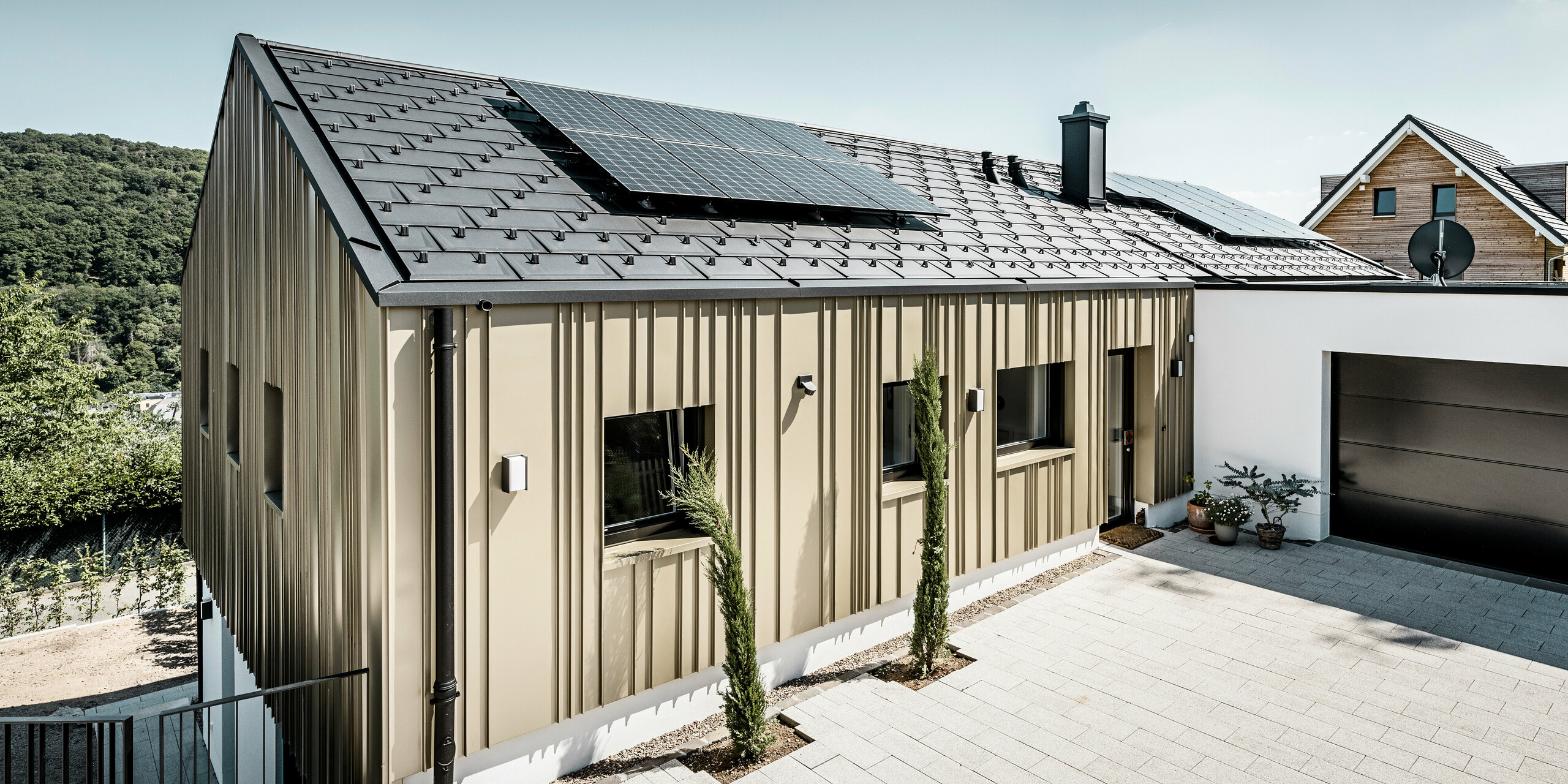 Ein Neubau in Bad Münstereifel wurde eingedeckt mit der PREFA Dachplatte R.16 in anthrazit. Auf dem Dach befindet sich eine Photovoltaik-Anlage. Die Winkelfalzfassade besteht aus Falzonal in lichtbronze.