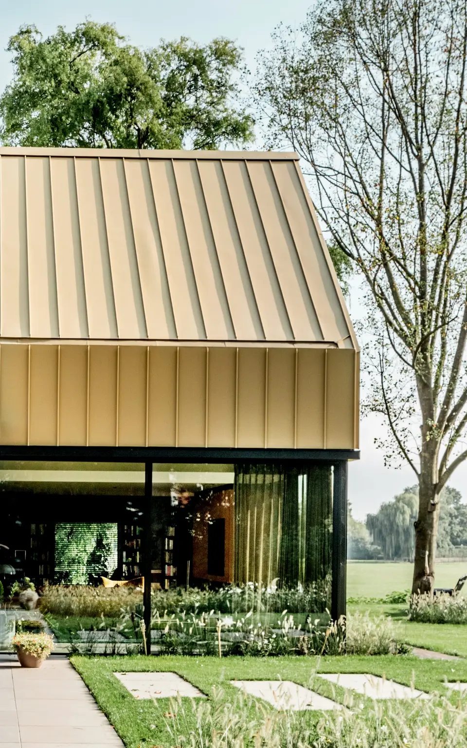 Moderne Architektur mit goldfarbenem PREFA Band- und Blechmaterial, das sowohl die Fassadenverkleidung als auch das Dach des Gebäudes prägt. Die präzise Verarbeitung und das hochwertige Design unterstreichen die vielseitigen Einsatzmöglichkeiten der PREFA Produkte für anspruchsvolle Architekturprojekte. Das Bild zeigt die perfekte Kombination aus Ästhetik und Funktionalität im "Goldenen Haus".
