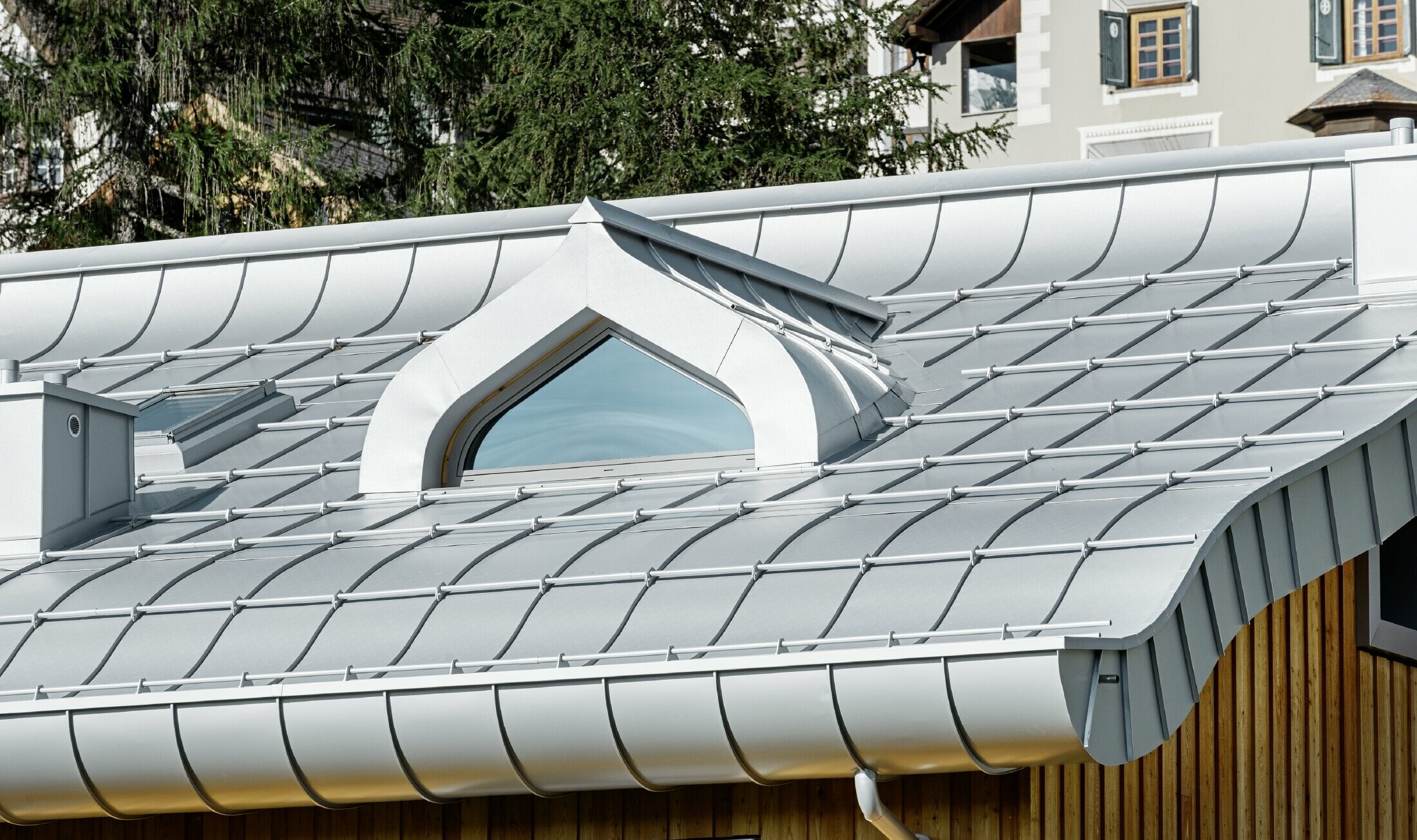 Wohnhausanlage in St. Moritz mit Holzfassade und Aluminiumdach mit geschwungener Traufe in silbermetallic