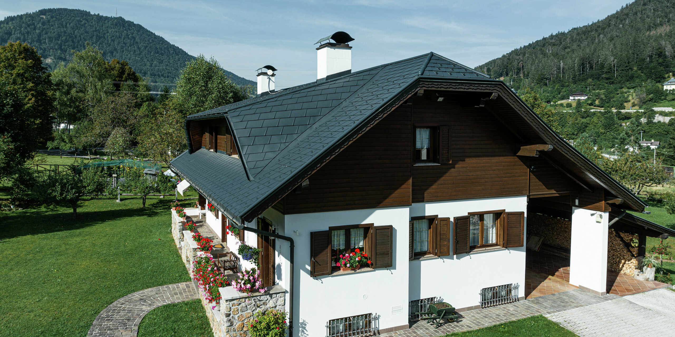 Inmitten der idyllischen Berglandschaft von Tarvis (Italien) wurde dieses Einfamilienhaus mit einer hochwertigen PREFA Dacheindeckung aus Aluminium modernisiert. Die anthrazitfarbenen PREFA Dachschindeln verleihen dem Gebäude nicht nur eine elegante Optik, sondern bieten auch dauerhaften Schutz vor Wind und Wetter. Die markante Hechtgaube fügt sich harmonisch in die Architektur ein und sorgt für zusätzlichen Wohnkomfort im Dachgeschoss. Holz- und Steinelemente runden das traditionelle Gesamtbild perfekt ab.