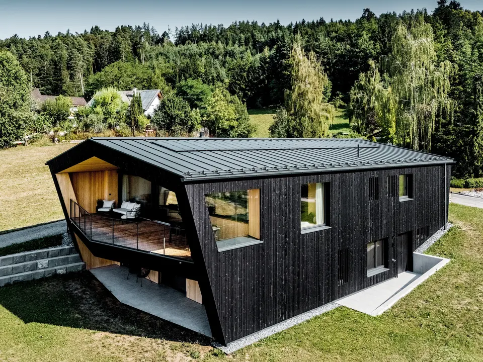 Dieses moderne Einfamilienhaus in Röthis besticht durch sein markantes Satteldach aus PREFALZ in der Farbe P.10 Anthrazit. Auf dem Dach thront zusätzlich das Solarmodul PREFALZ für nachhaltige Energiegewinnung. Die dunkle Holzfassade, die großzügigen Fenster und der außergewöhnliche Balkon mit warmer Holzverkleidung schaffen spannende Kontraste. Die langlebige, leichte und witterungsbeständige PREFA Aluminiumdeckung sowie die farblich abgestimmte Dachentwässerung vereinen moderne Architektur mit zuverlässiger Funktionalität.