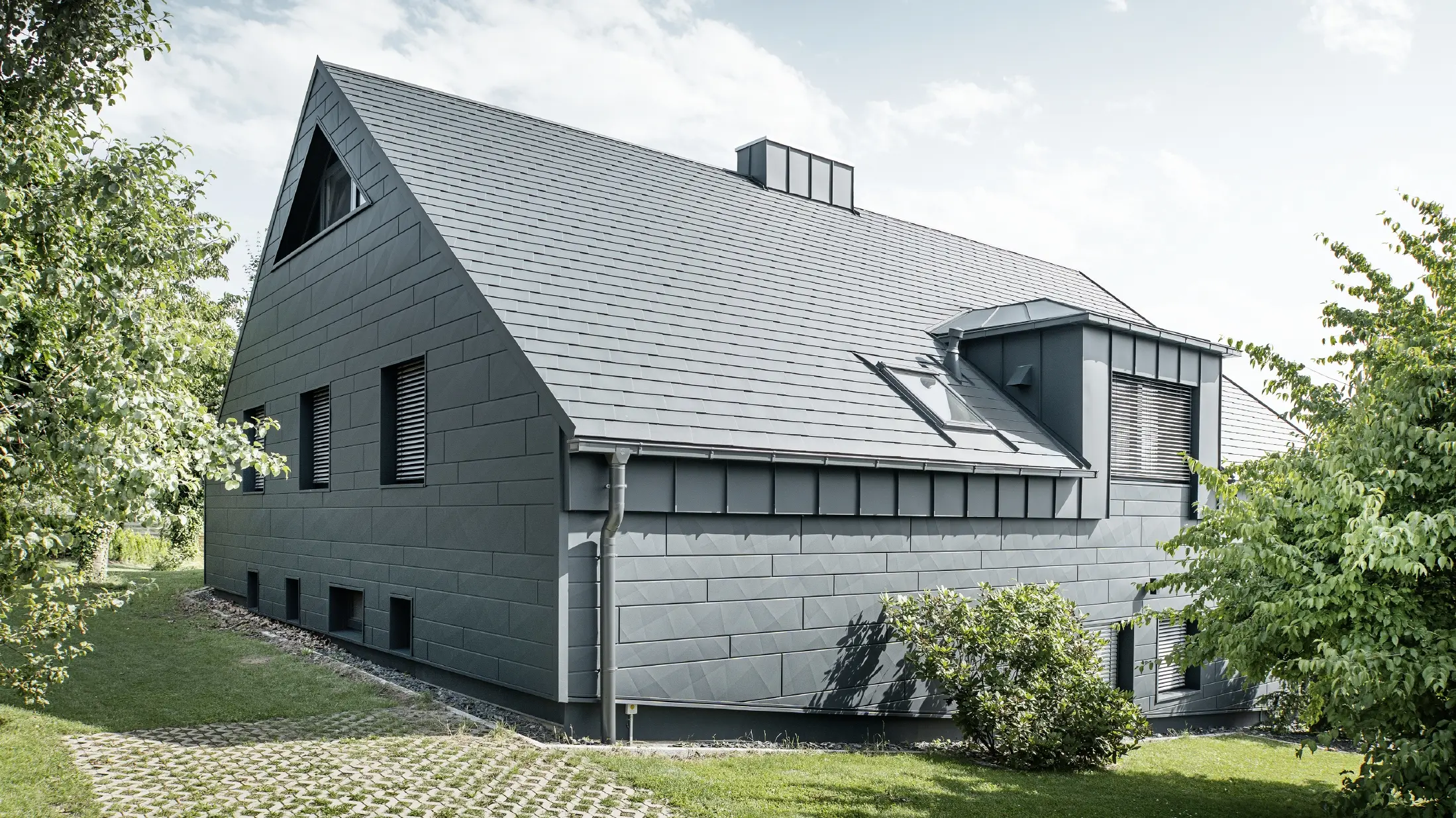 Großes Einfamilienhaus mit Satteldach und vielen Fenstern. Das gesamte Haus wurde mit einer Aluminiumhülle in Anthrazit verkleidet, am Dach kamen PREFA Alu-Dachschindeln zum Einsatz und an der Fassade Siding.X in Anthrazit.