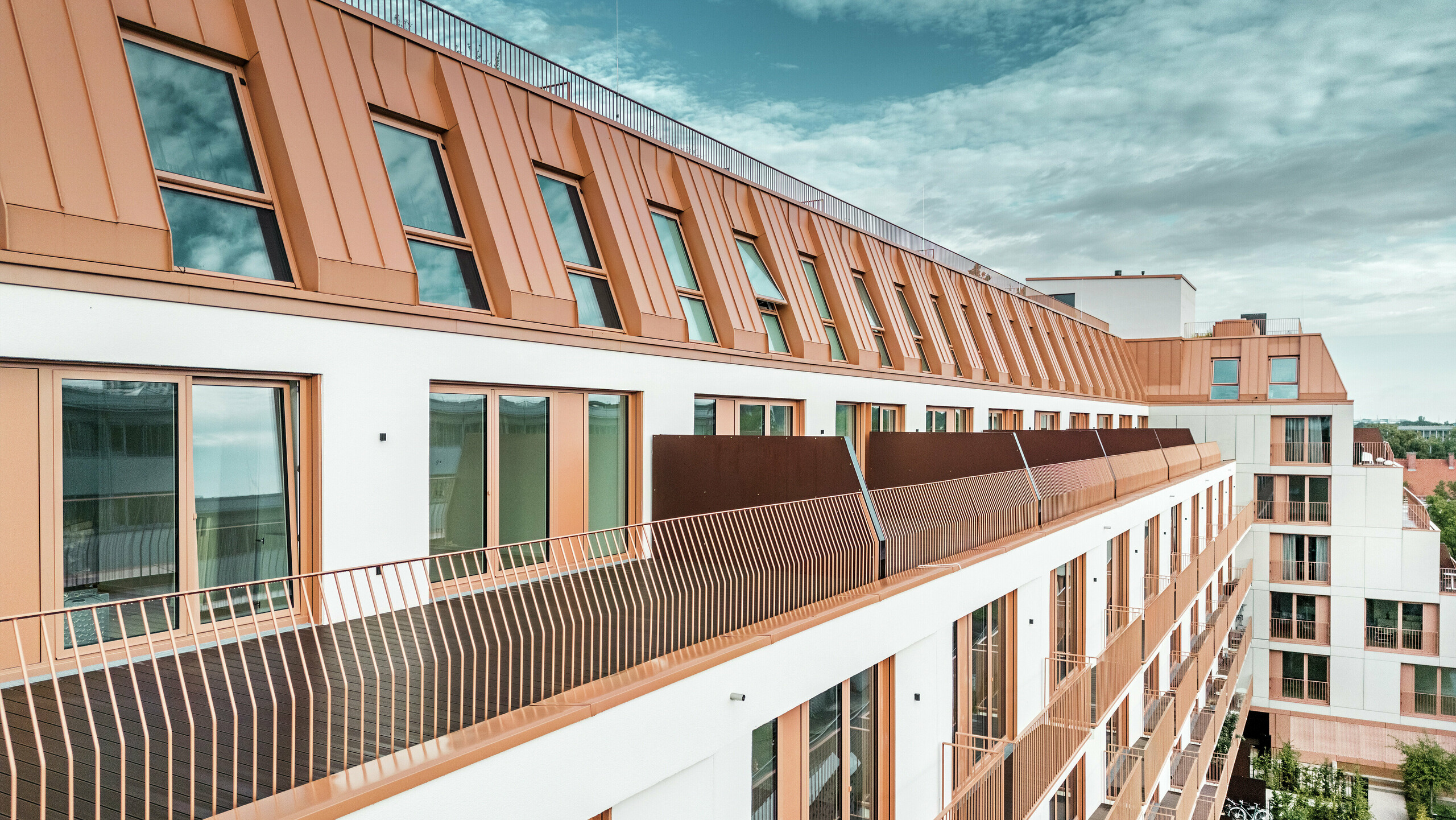 Modernes Wohnhaus Van B in München mit markanter Dachlandschaft aus PREFALZ Aluminium in der Sonderfarbe IGP Orange HDP. Die langlebige und wartungsarme Dacheindeckung von PREFA sorgt für ästhetische Einheit und hohe Witterungsbeständigkeit. Die elegante Fassadengestaltung mit kupferorangenen Fensterrahmen und großzügigen Balkonflächen unterstreicht das innovative Architekturkonzept. Die ideale Lösung für urbane Bauprojekte mit Anspruch an Design und Funktionalität.