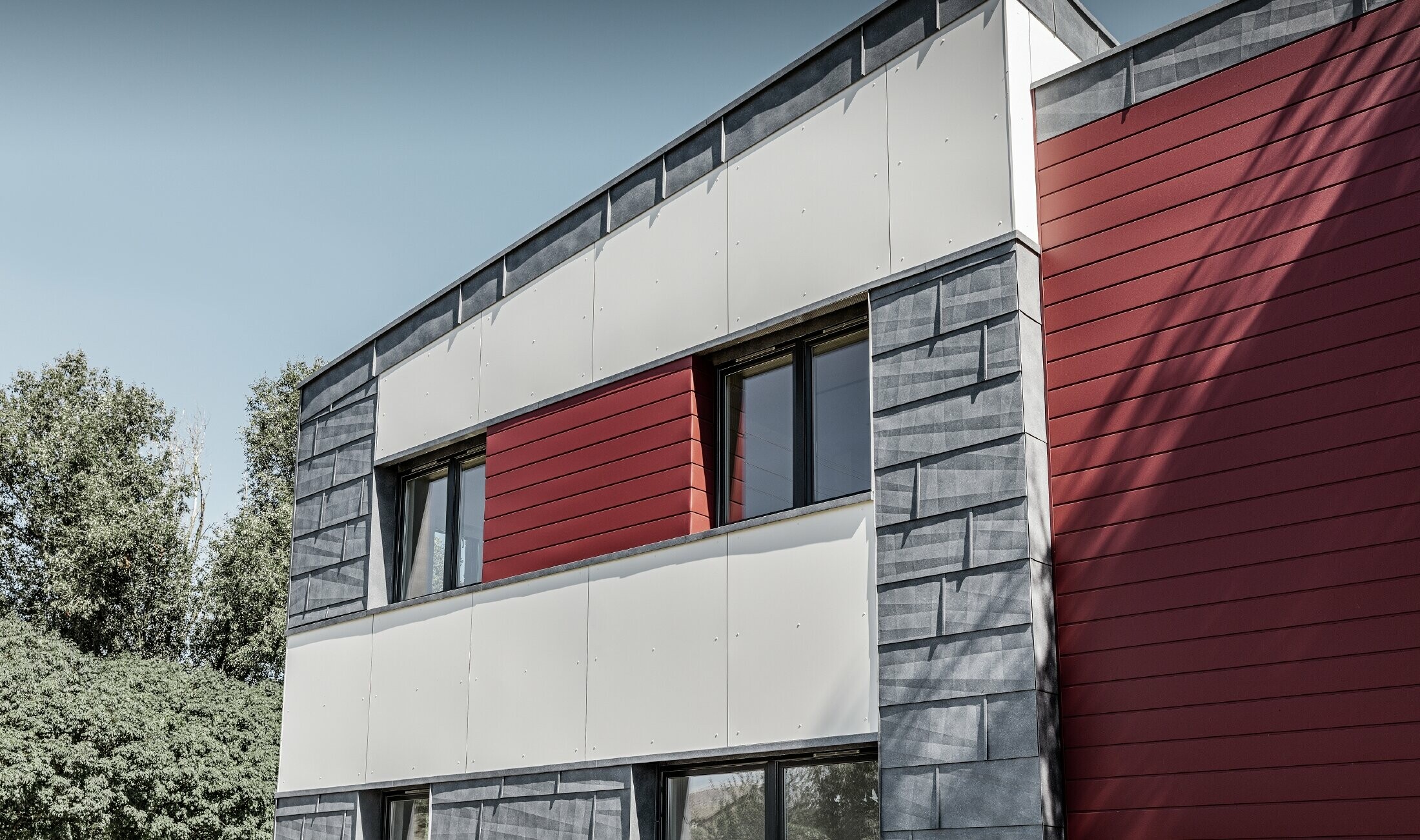 Modernes Bürogebäude mit einer geteilten Fassade in rot, steingrau und weiß mit Aluminiumprodukten Sidings, Fassadenpaneel FX.12 und Aluminium Verbundplatte von PREFA