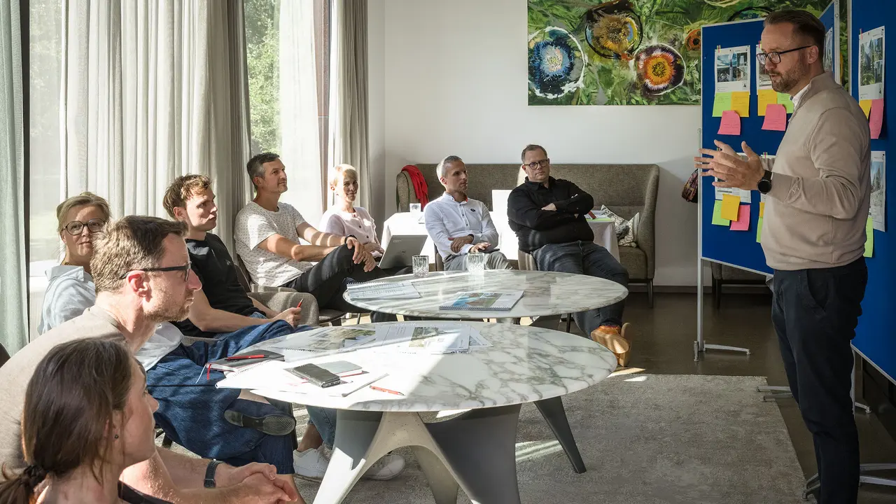 Expertenjury diskutiert in einer Winzerresidenz im burgenländischen Seewinkel über Architekturobjekte für das PREFARENZEN Buch und den Kalender 2027; ein Mann präsentiert vor Pinnwänden, während die Jury aufmerksam zuhört.