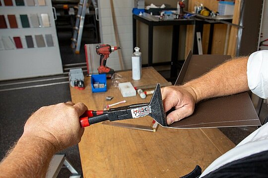 Der PREFA Techniker demonstriert mit einer Quetschfalzzange, wie er die erste Falte der Fensterbank nach hinten kantet.