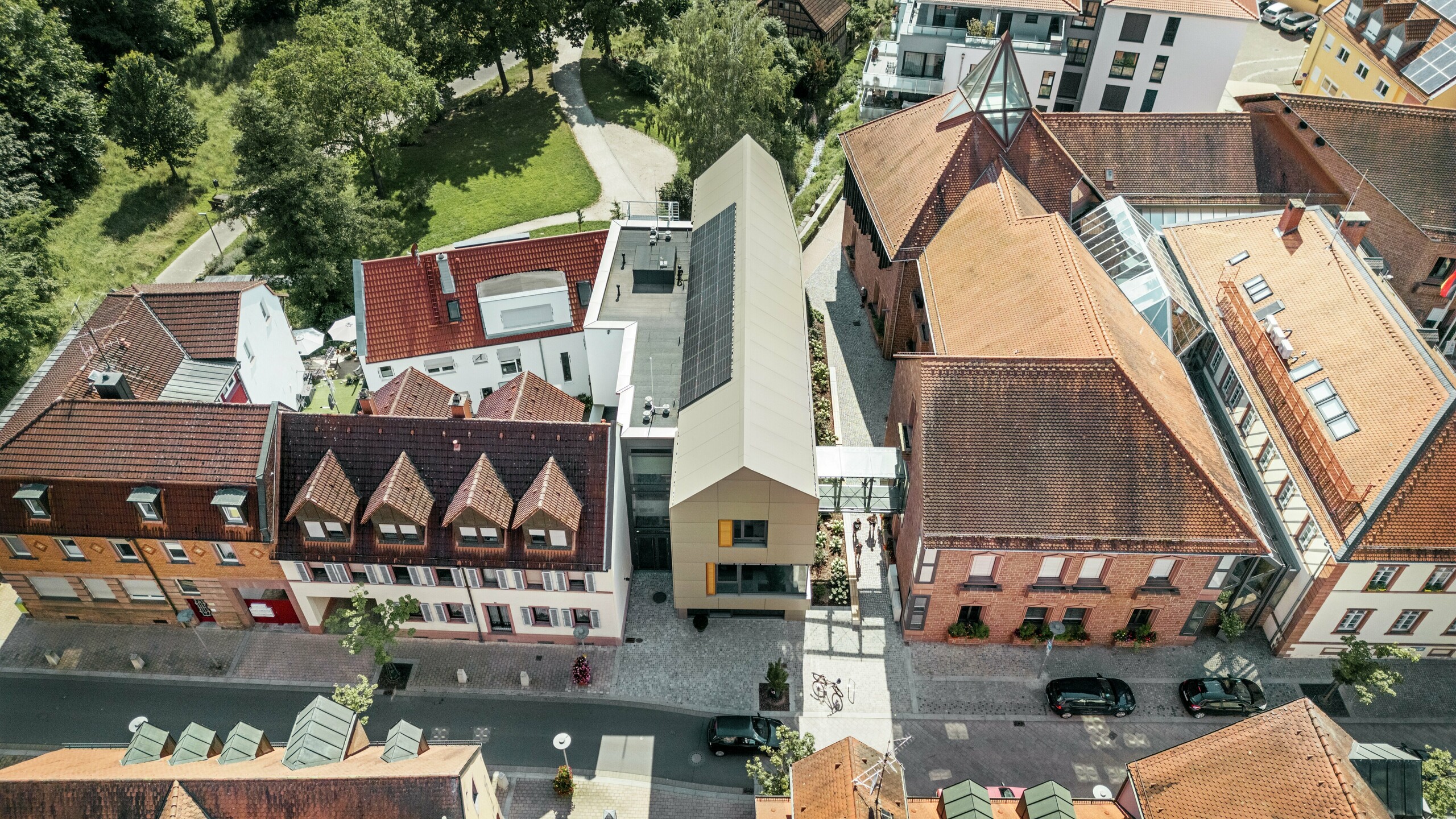 Das Rathaus in Alzenau, Deutschland, befindet sich im Zentrum einer historischen Stadtlandschaft, umgeben von traditionellen Gebäuden mit roten Ziegeldächern. Im Kontrast dazu steht das moderne Rathaus, dessen Fassade mit Aluminium-Verbundplatten von PREFA in einem eleganten Bronze-Ton verkleidet ist. Die innovative Architektur hebt sich klar von den benachbarten, klassischen Gebäuden ab und fügt sich dennoch harmonisch in das Stadtbild ein.