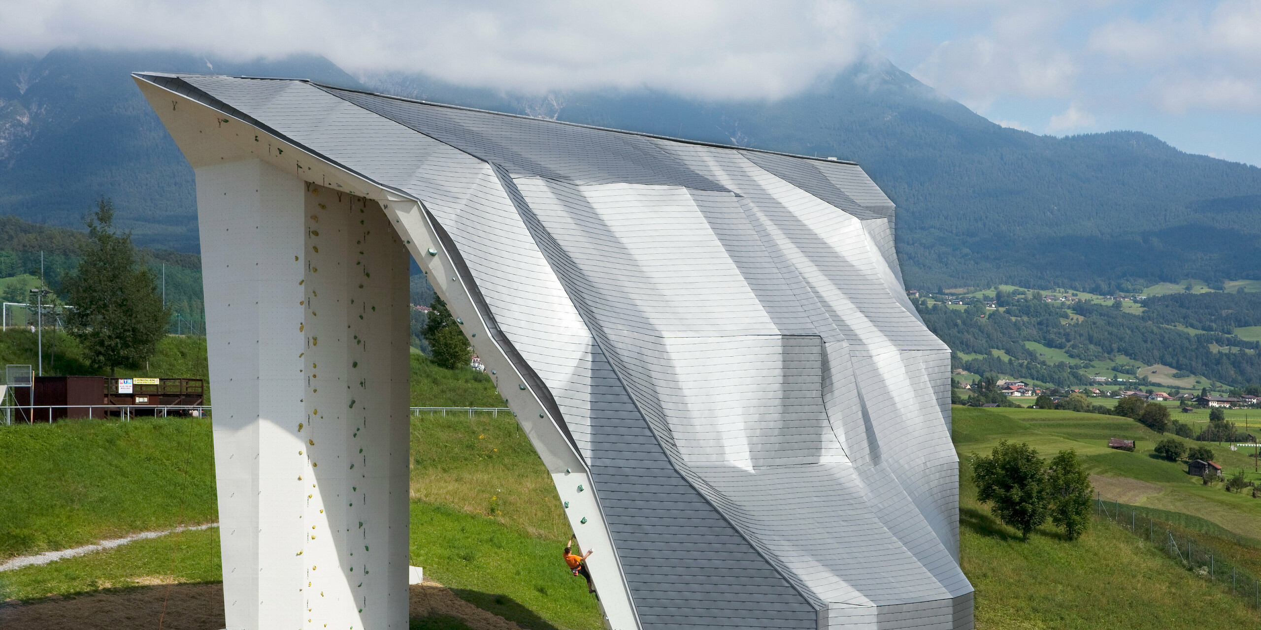 Vogelperspektive auf den Kletterturm Imst mit Aluminiumdach bzw. -fassade aus PREFA Dachschindeln in Silbermetallic und Bergpanorama im Hintergrund