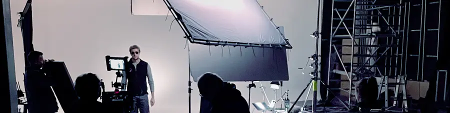Blick hinter die Kulissen einer Fotosession für PREFA, mit einem männlichen Model in Sonnenbrille und PREFA-Weste, der zentral vor einer weißen Leinwand steht. Die Szene wird über Monitore abgebildet, die für die Aufnahmekontrolle verwendet werden, mit Beleuchtungsausrüstung und Crewmitgliedern im Hintergrund, die die Produktion steuern. Das Bild wurde im Zuge der PREFA Werbekampagne 2024 aufgenommen. Die Kampagne läuft unter dem Credo „Unsere starken Produkte und unsere Handwerkspartner:innen: ein unschlagbares Paket!“.